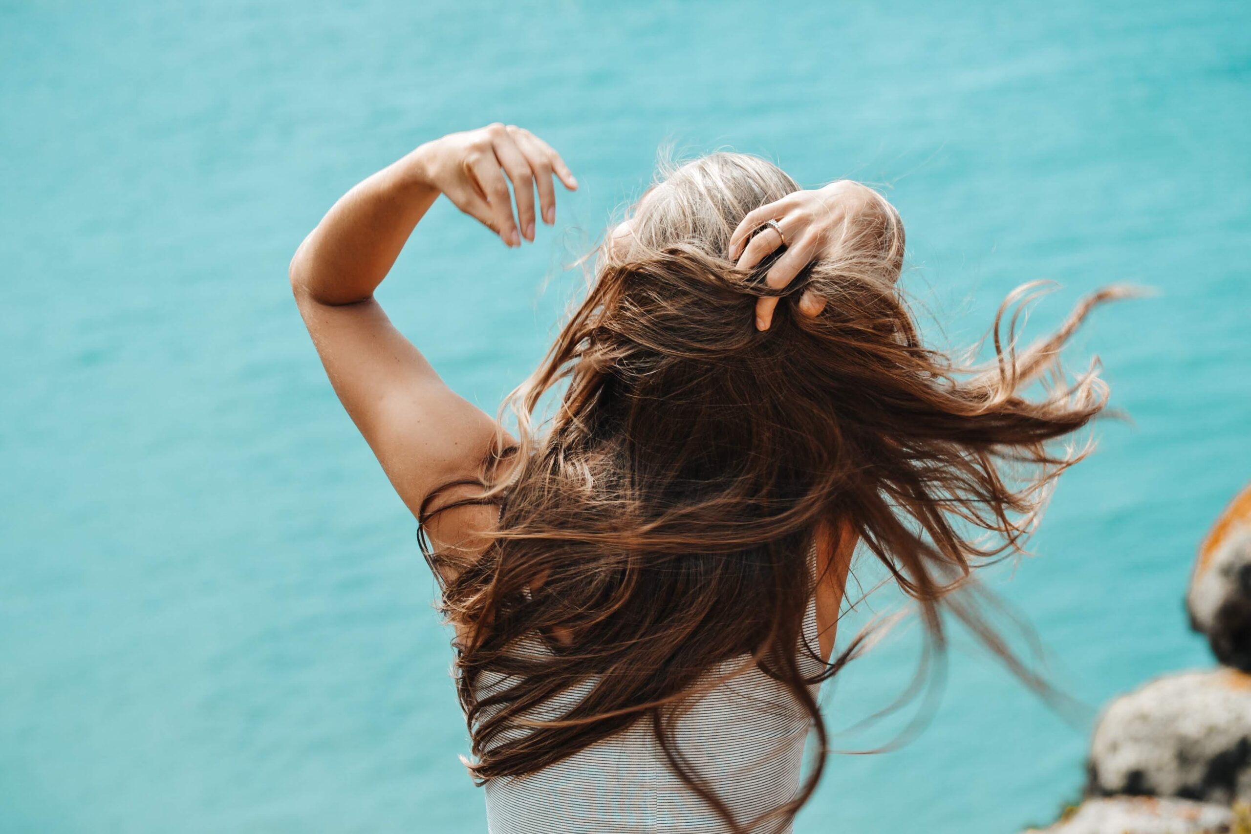 A woman brushing her hair with her hands on a windy shore.