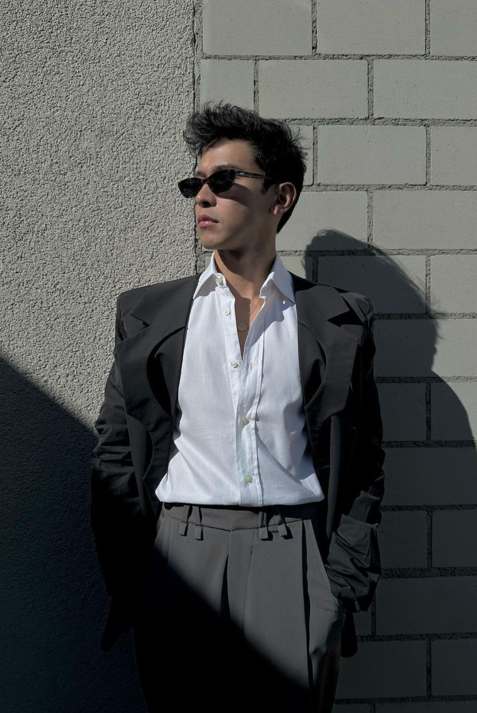 The actor is wearing an Ellis Co deconstructed black and gray suit ensemble