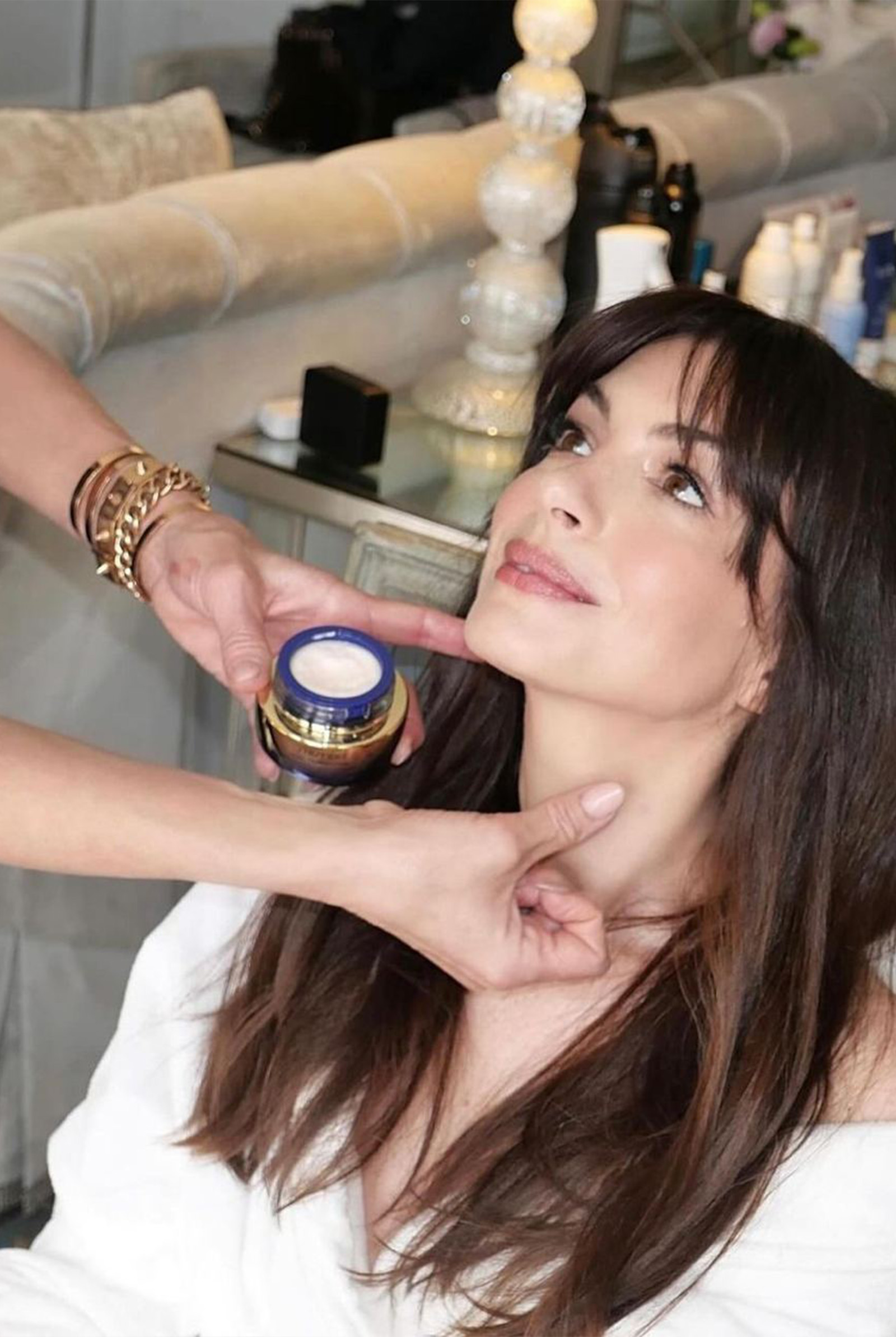 Anne Hathaway looking at her makeup artist with the Shiseido VITAL PERFECTION jar near her face