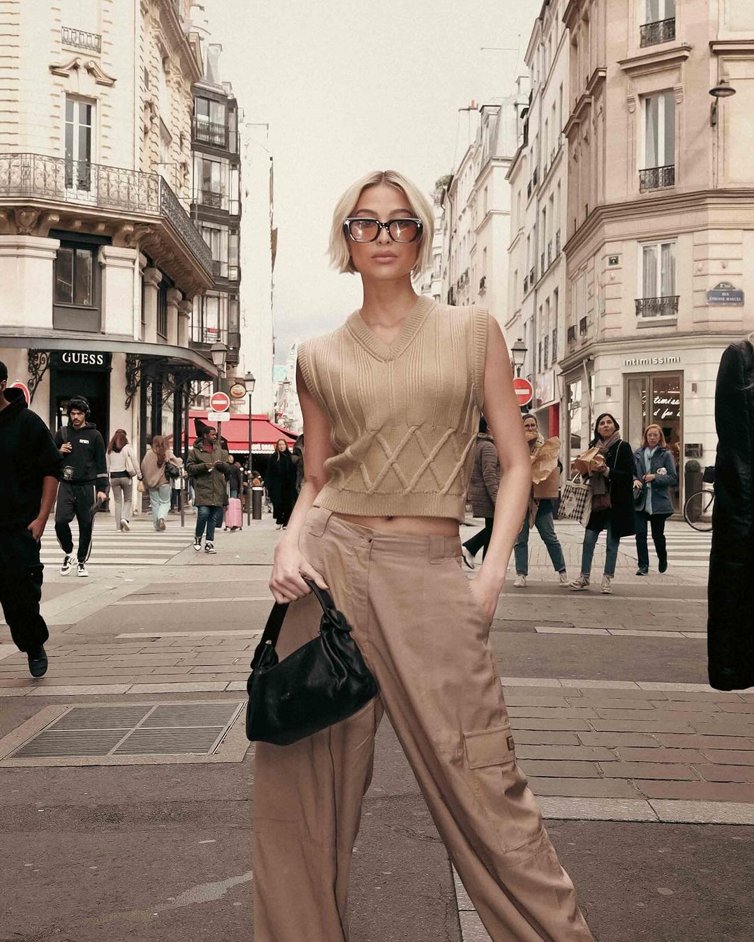 Michelle Dee wearing Kenzo: a knitted vest, cargo parachute pants, white boots, and a black leather bag during Paris Fashion Week