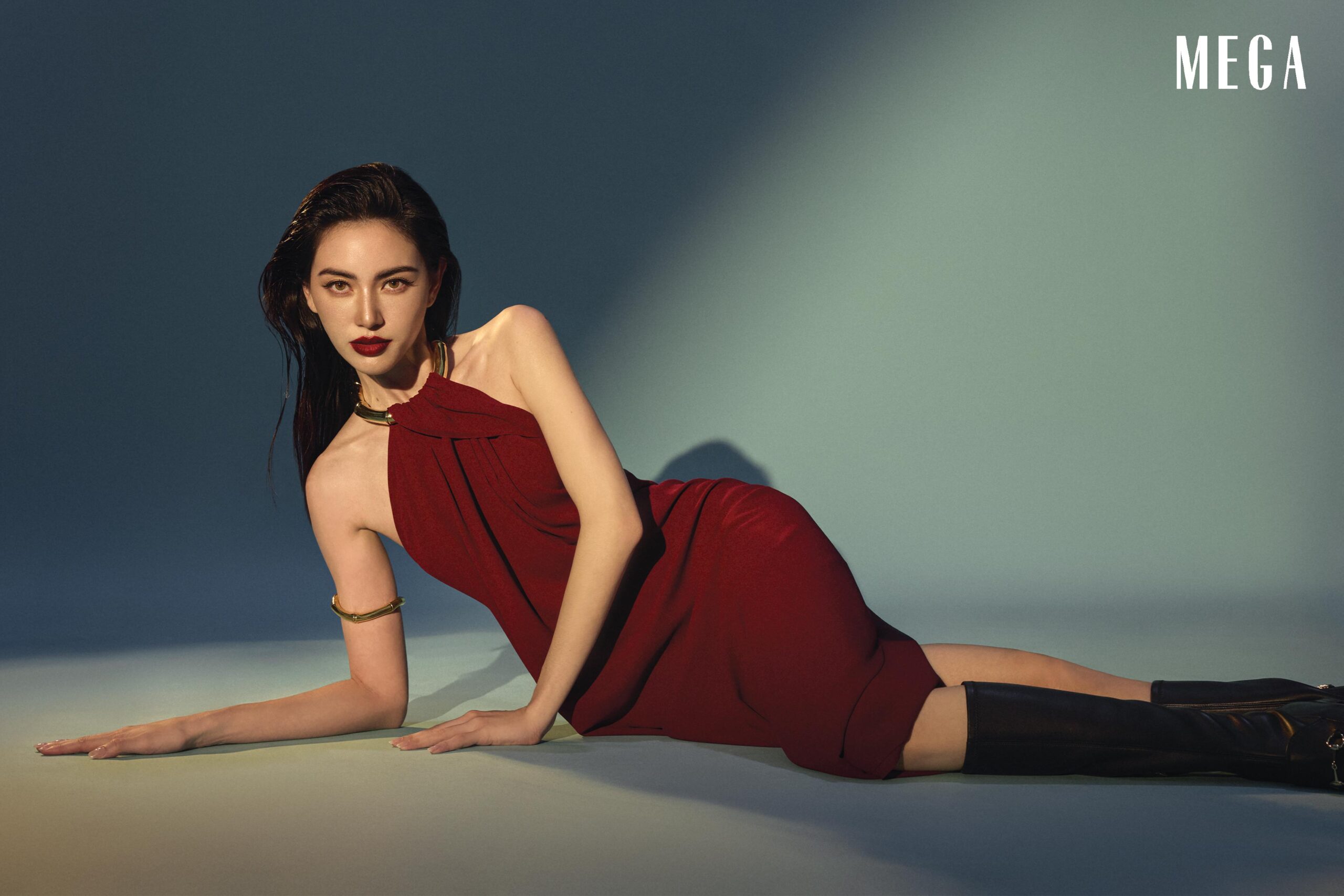 Davika Hoorne is wearing GUCCI Red sleeveless v-neck midi dress with bamboo necklace detail, GUCCI black knee high flat boots with horsebit detail, gold arm GUCCI bracelet