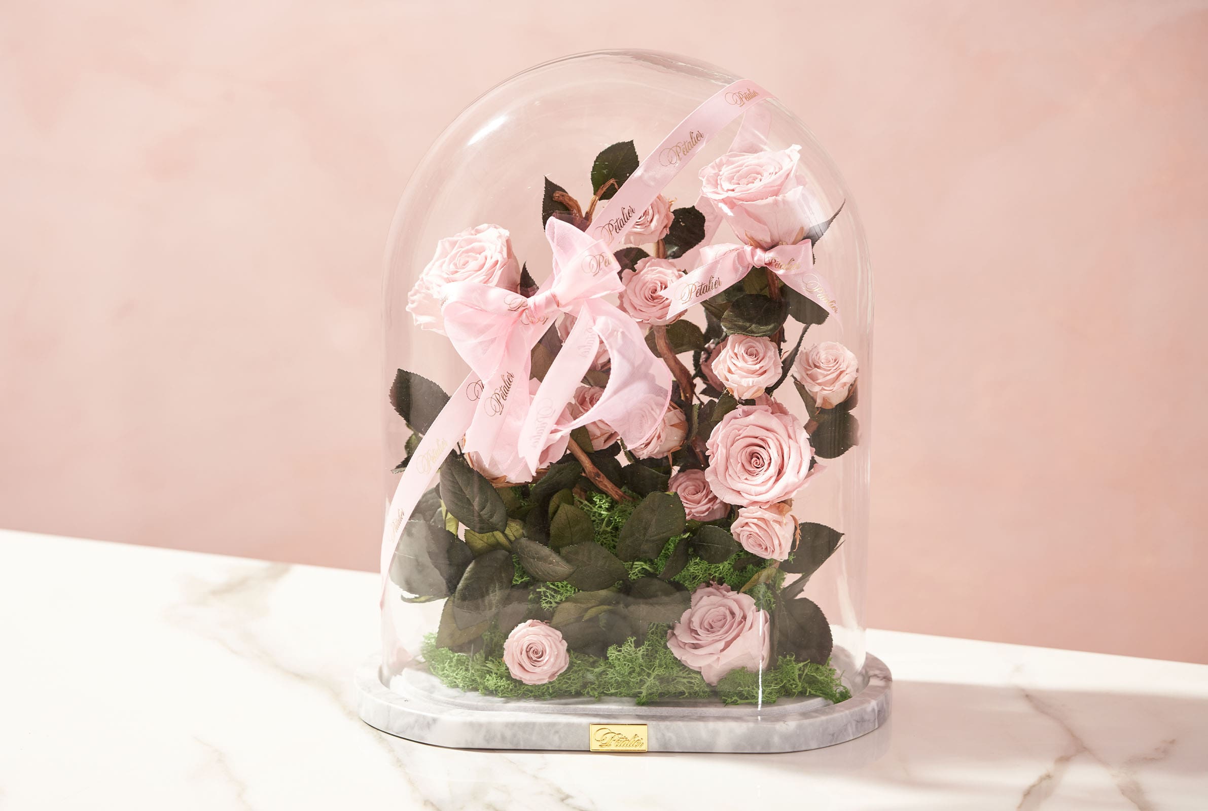 A pink arrangement of flowers encased in a dome by Petalier