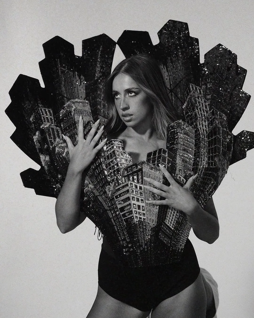 Black-and-white photo of a woman wearing a sculptural gown made from city-block shapes, resembling a skyline.
