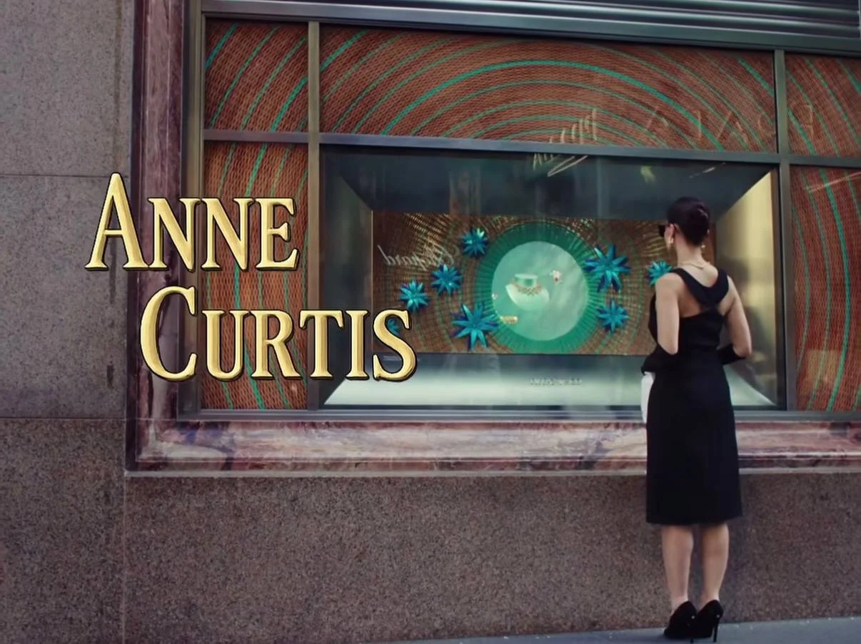 Woman in a black dress stands before a store display featuring a large Anne Curtis sign and teal circular art with blue starbursts.