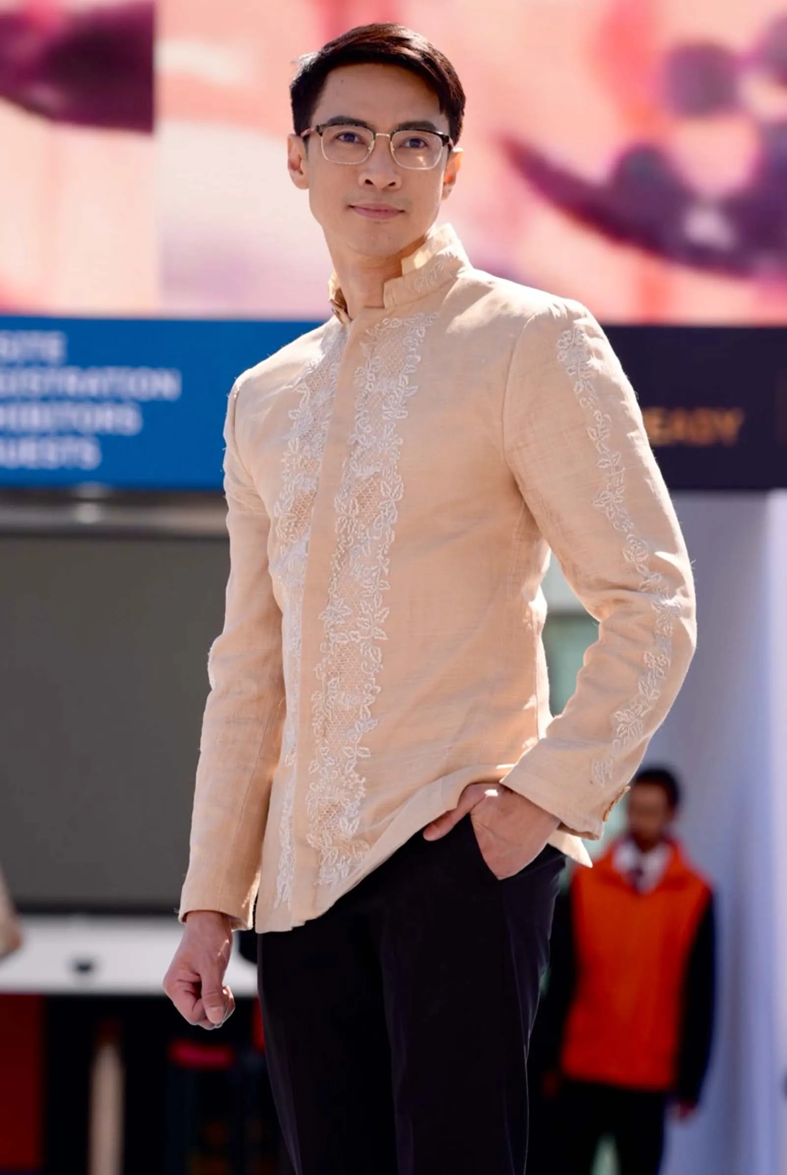Man wearing a beige embroidered kurta, standing with one hand in his pocket at an outdoor event