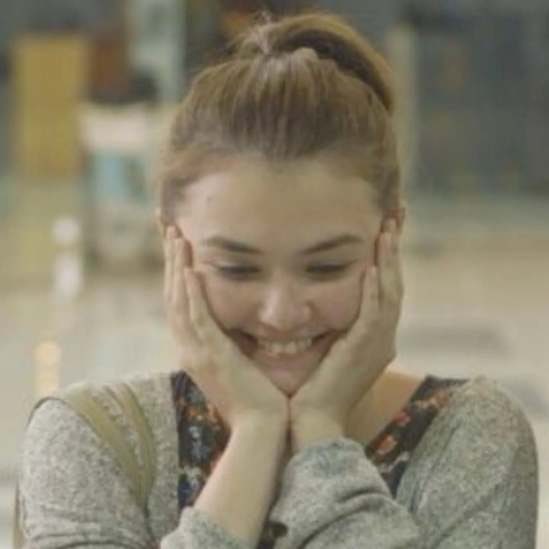 Close-up of a person smiling, with light brown hair tied back, wearing a gray knit sweater.