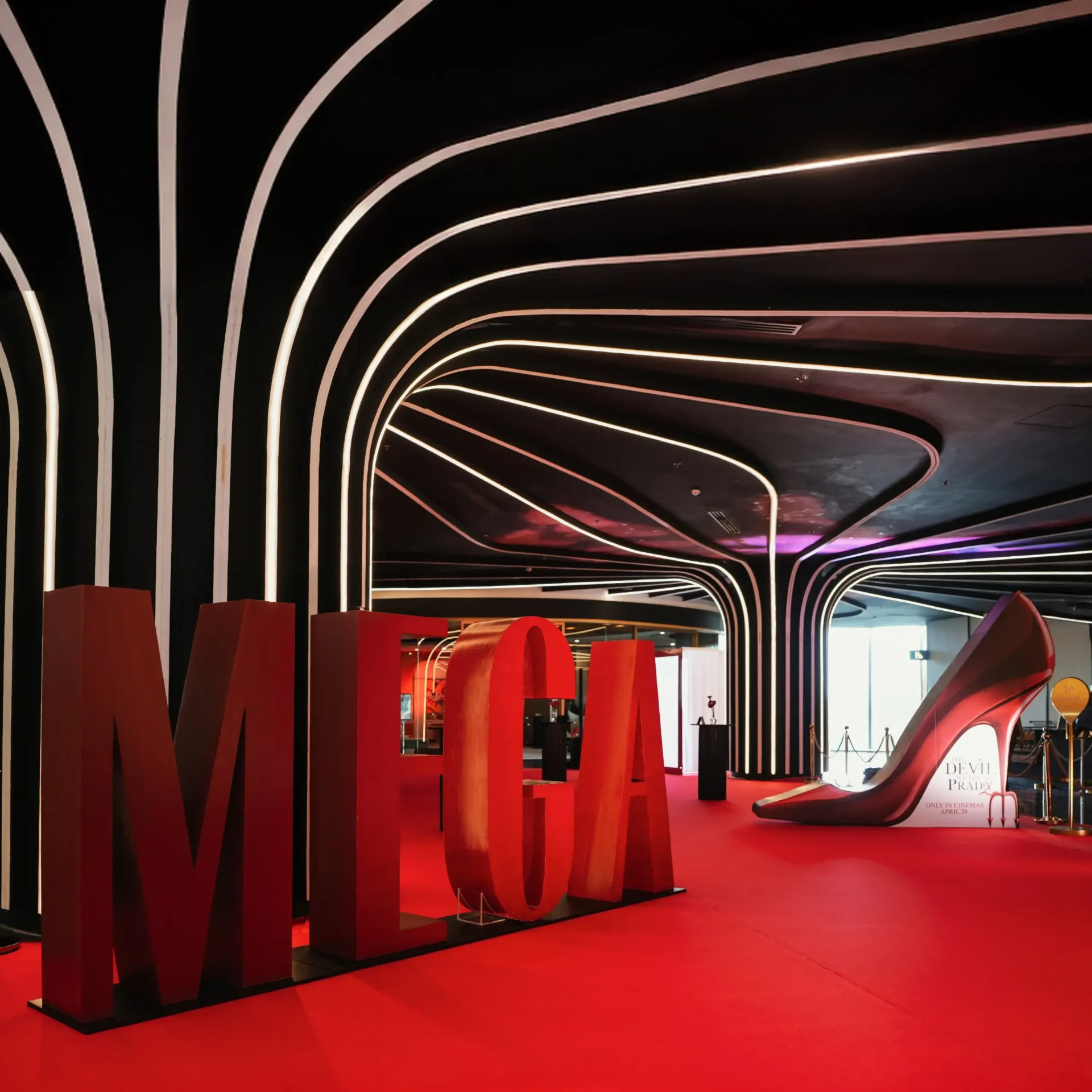 Oversized red letters spelling 'LOVE' standing as an art installation inside a modern exhibition space with a curved neon-lined ceiling and red carpet.