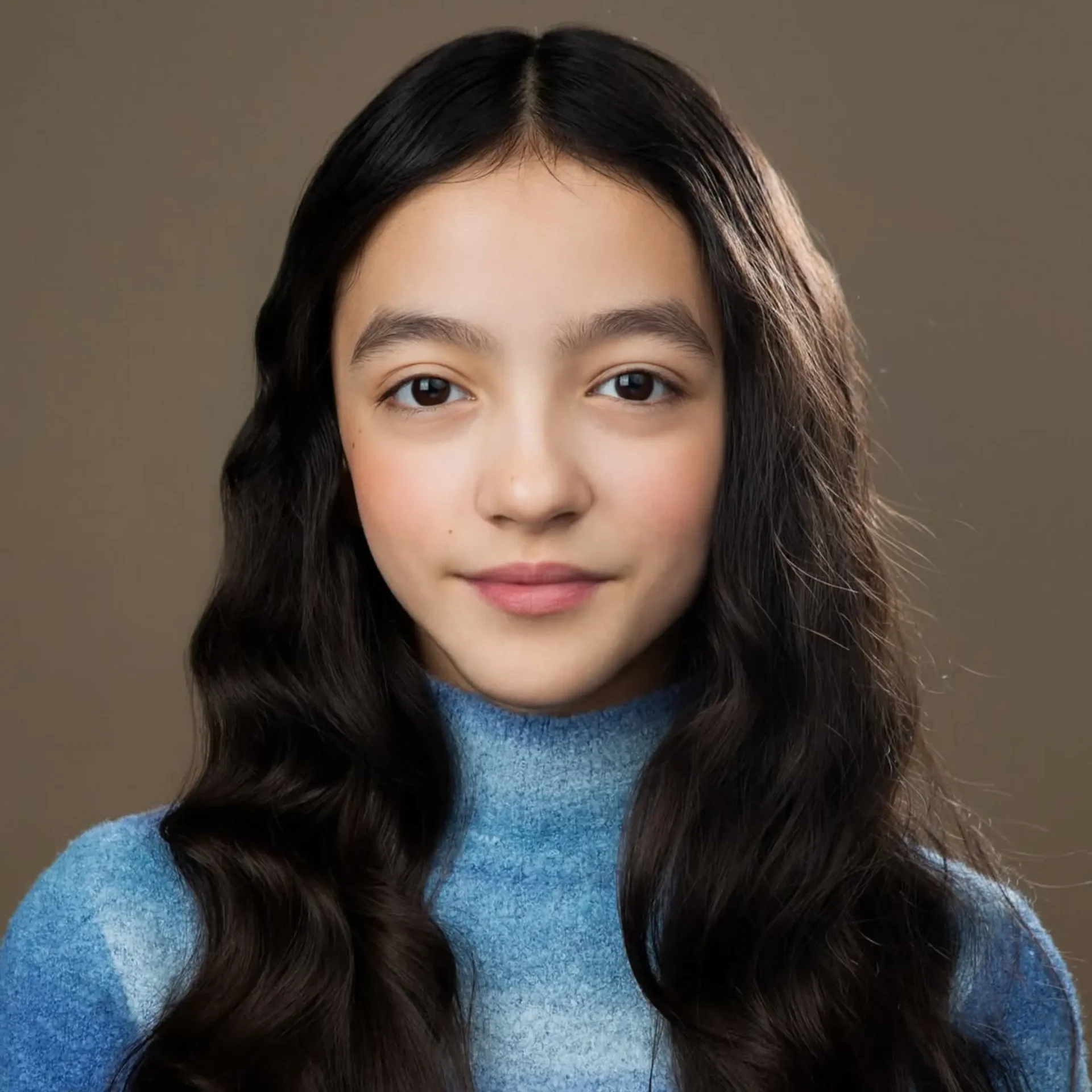 Portrait of a young girl with long, dark hair wearing a blue knit turtleneck, against a neutral brown background.