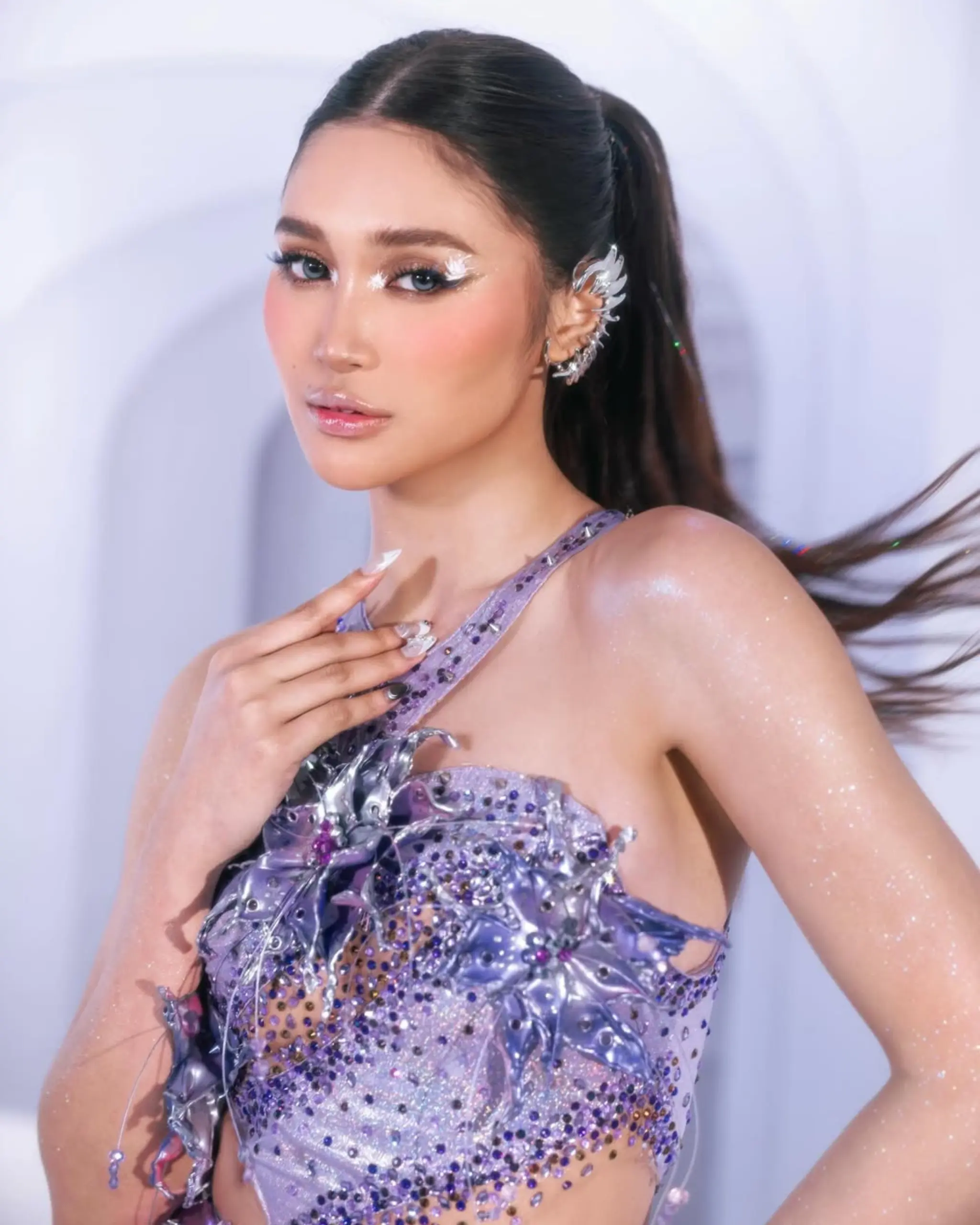 Glamorous woman posing in a sparkly lavender dress with rhinestones, her hair in a ponytail and silver ear accessory.