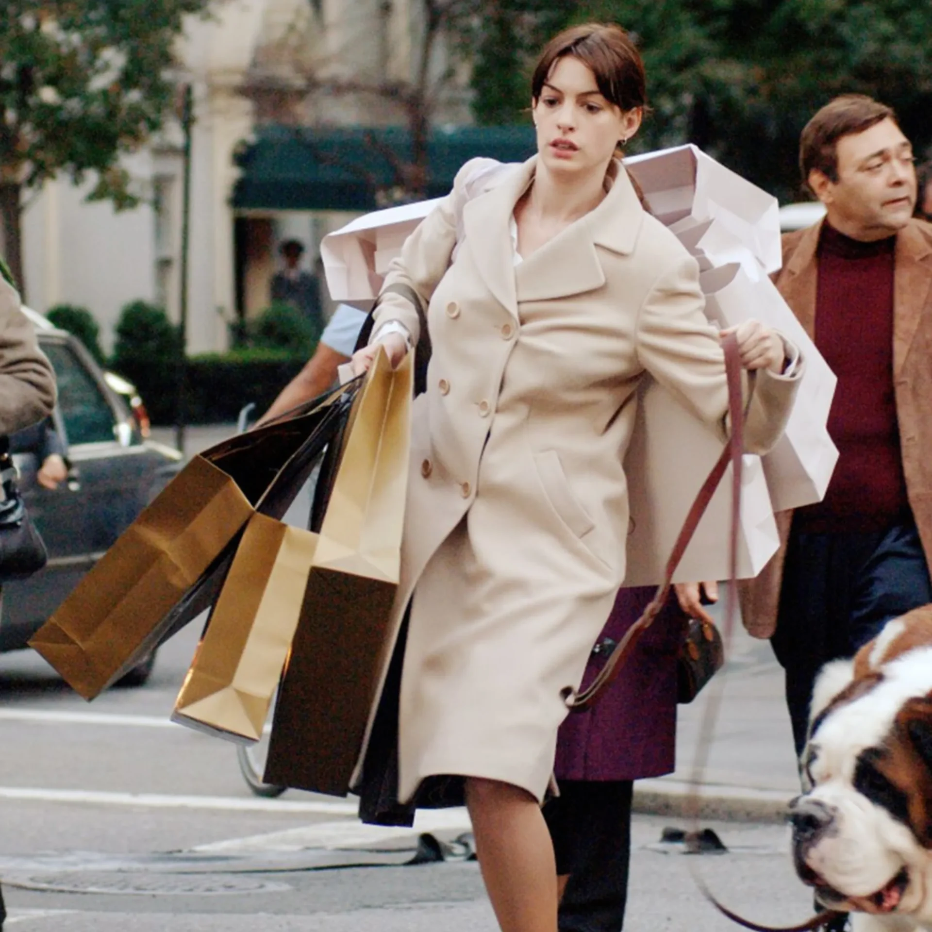 Woman in a light coat running on a city street with multiple shopping bags and a dog nearby on a leash.