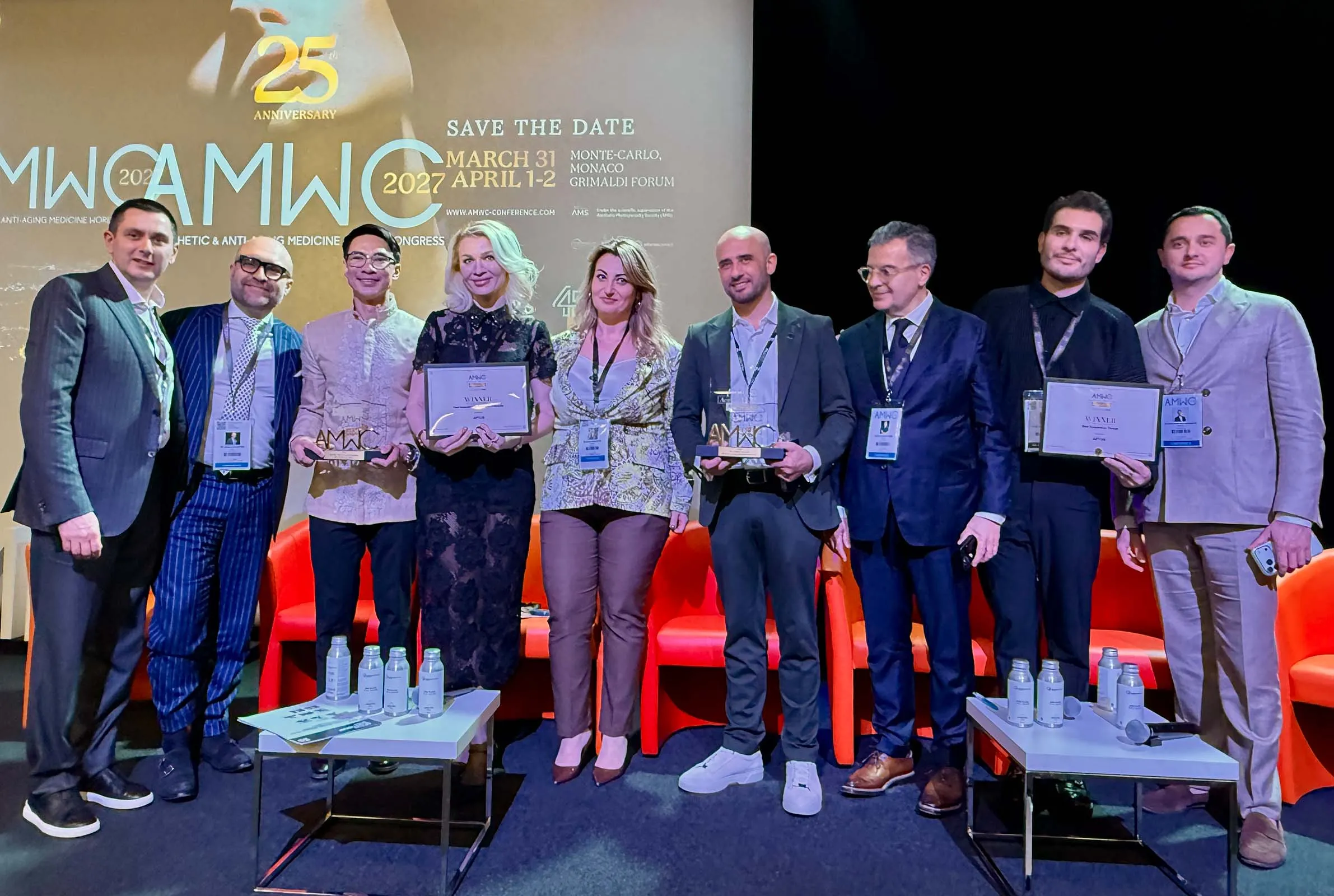 Group of eight professionals on a stage holding awards and certificates at an event.