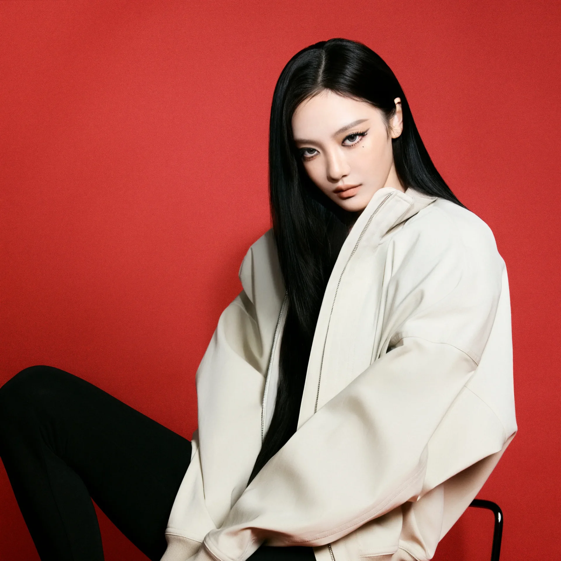 Portrait of a woman with long black hair and a light beige jacket against a solid red background. (informative)