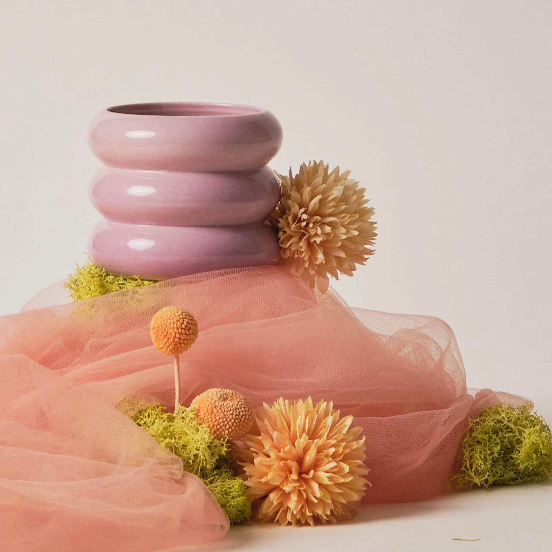 Pink tiered ceramic sculpture surrounded by peach flowers and pink tulle in a soft still life arrangement.