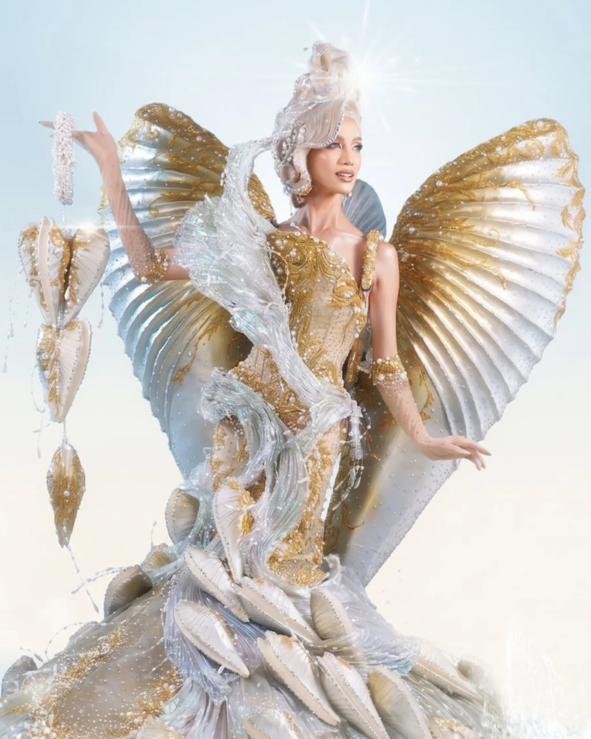 Dancer in an elaborate gold and white costume with big feathered wings, sparkling and luminous background.