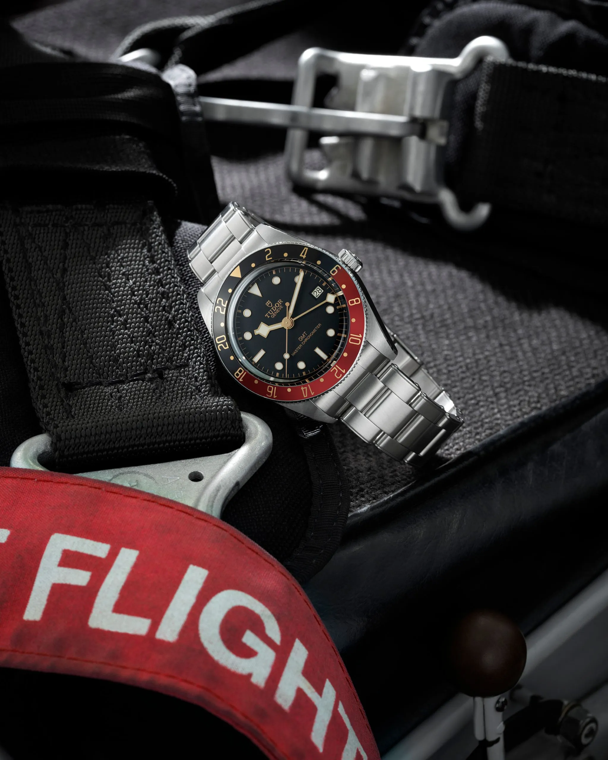 Tudor GMT stainless steel watch with a red and black bezel resting on tactical gear.