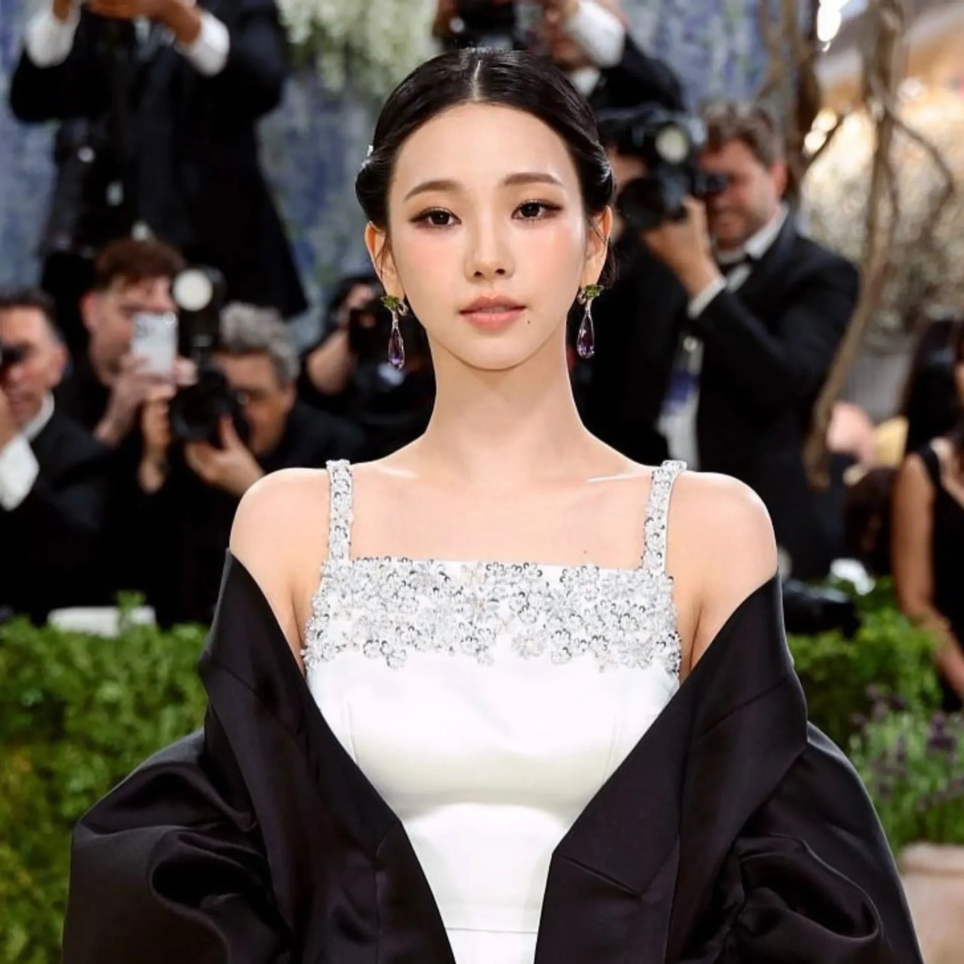 Young woman in a silver beaded dress posing for cameras with photographers in the background.