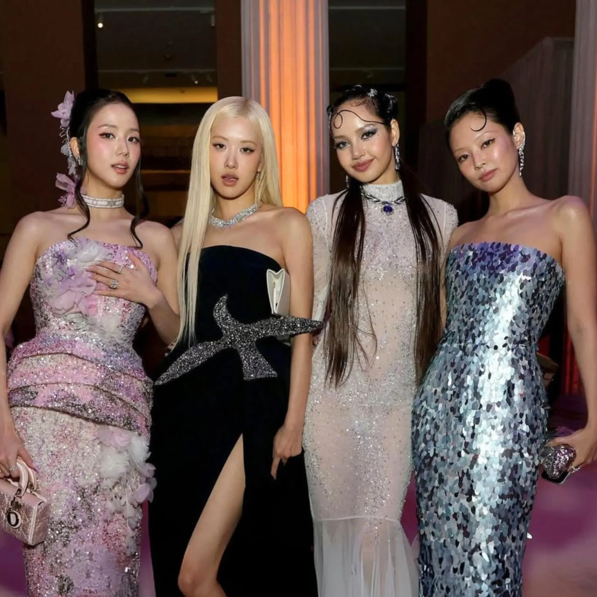 Four women in formal gowns posing together at an event, wearing sparkling dresses and jewelry.