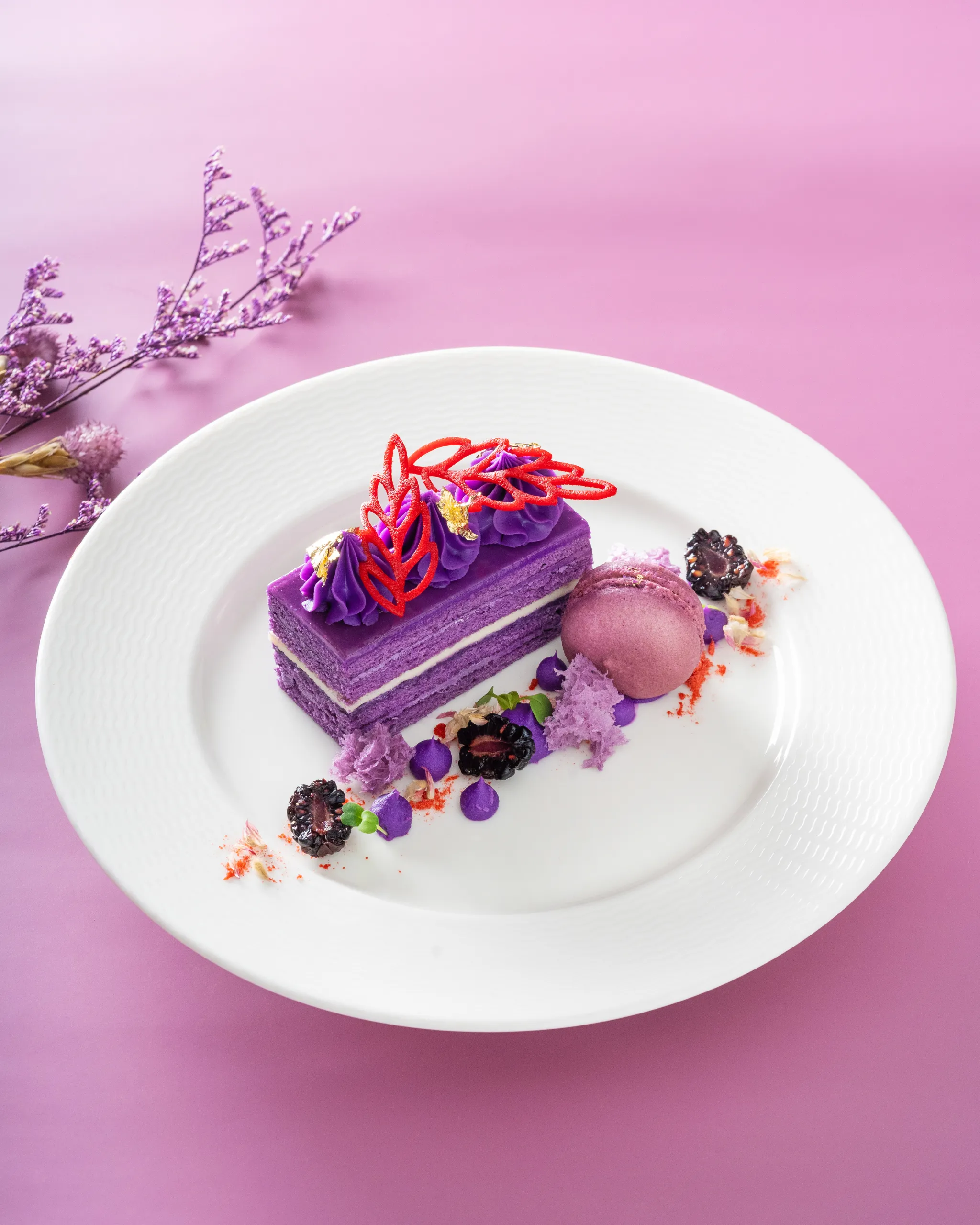 Purple-frosted pastries on a white plate with a pink background and dried purple flowers nearby.