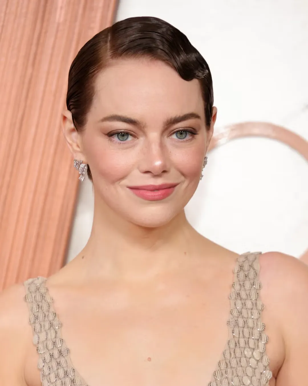 Close-up of a woman with dark, slicked-back hair wearing a beaded beige dress, smiling at the camera at a formal event.