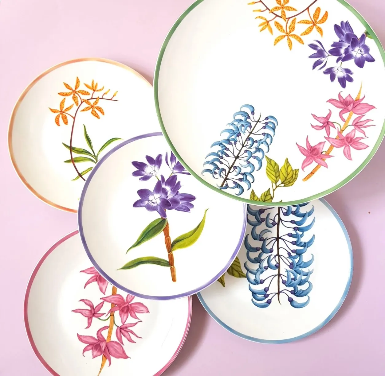 Set of decorative ceramic plates with colorful floral prints laid on a pink background. casa juan Bulaklak collection
