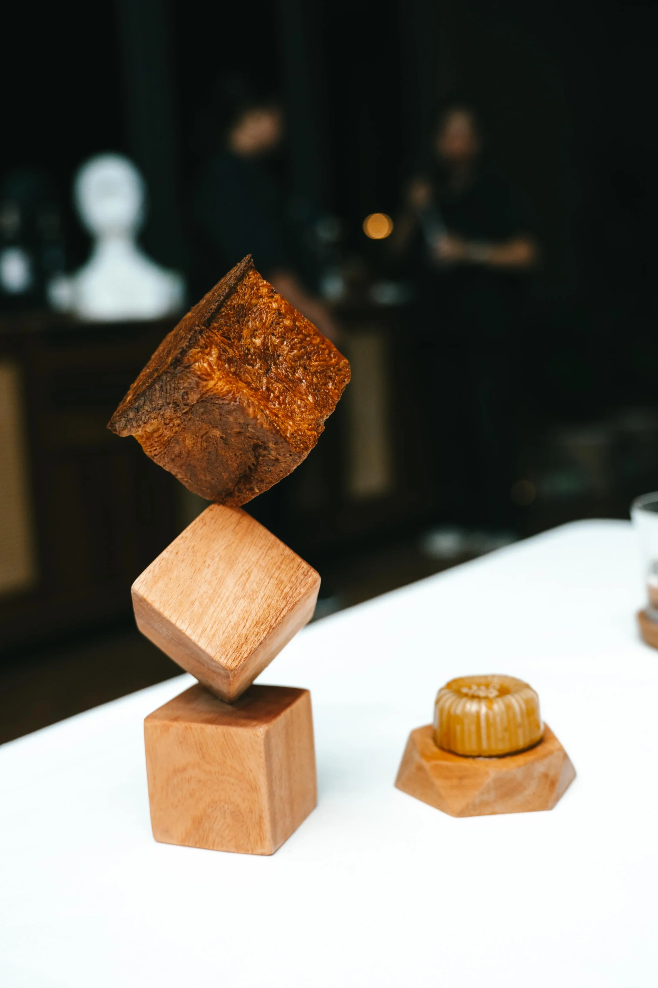Brown rock candy cube balanced on stacked wooden blocks, with a blurred dark background.