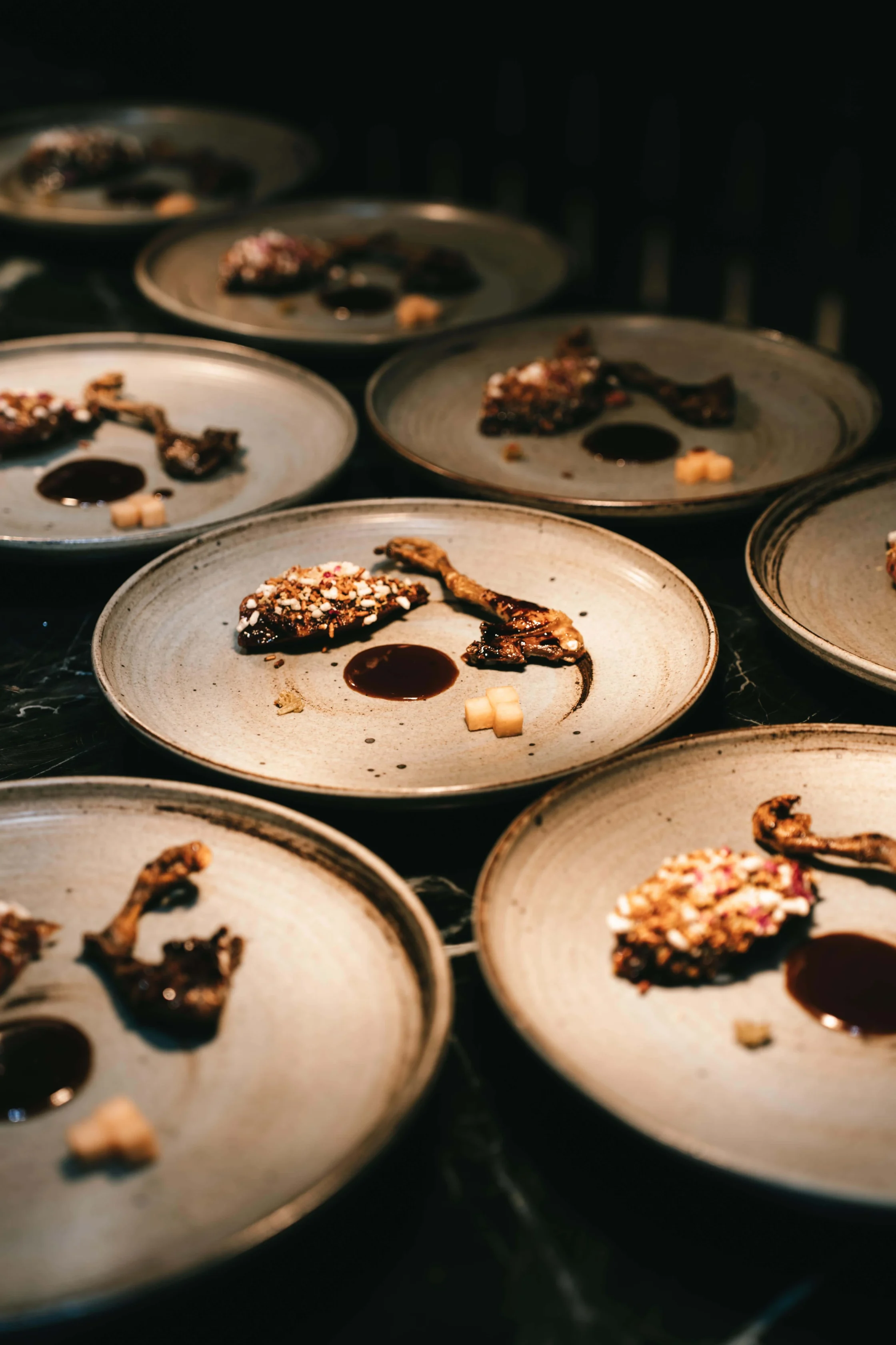 Close-up of round metal plates holding small chocolate dessert bites, topped with nuts, in a dim kitchen setting.