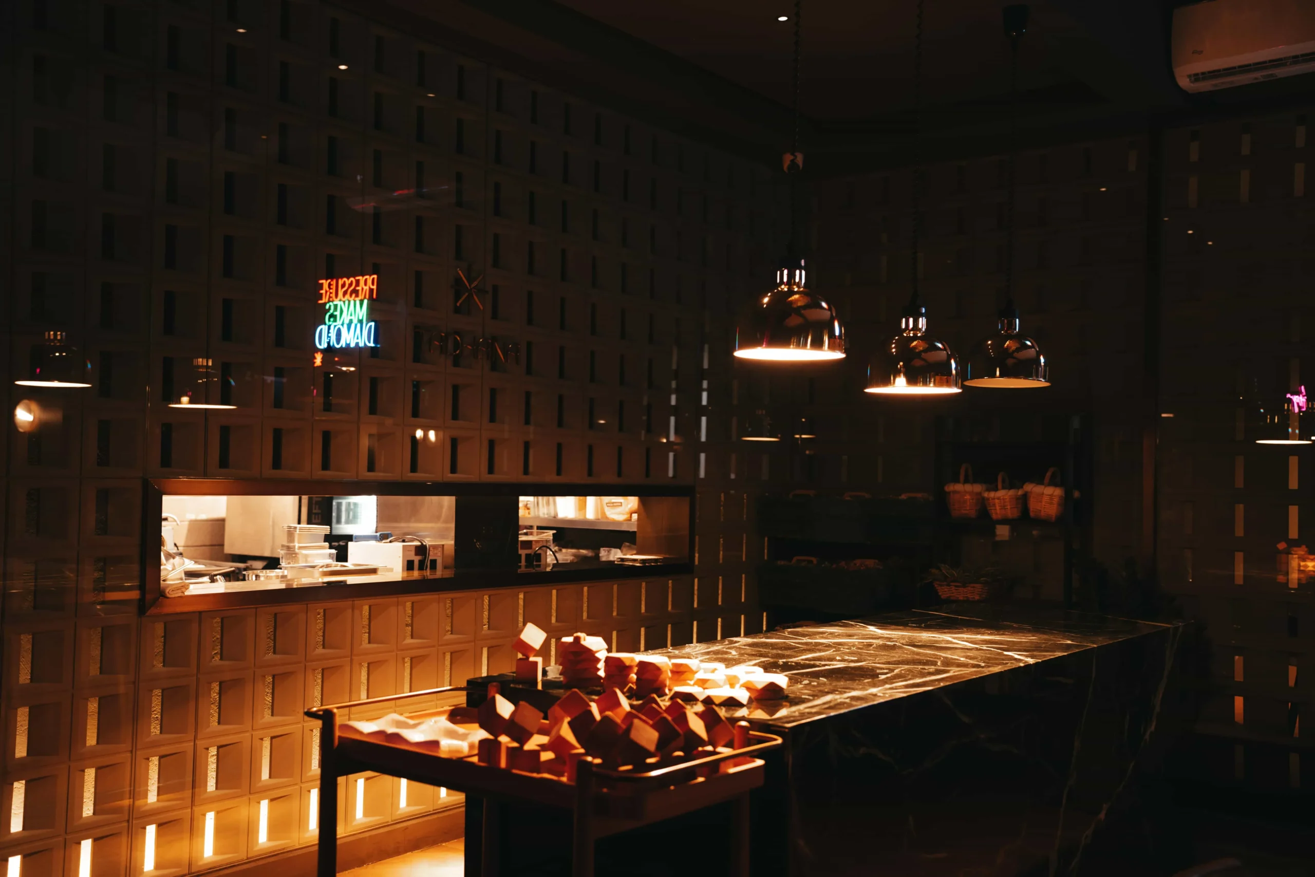 Dimly lit bakery interior with a marble display counter filled with pastries and warm copper pendant lights overhead.