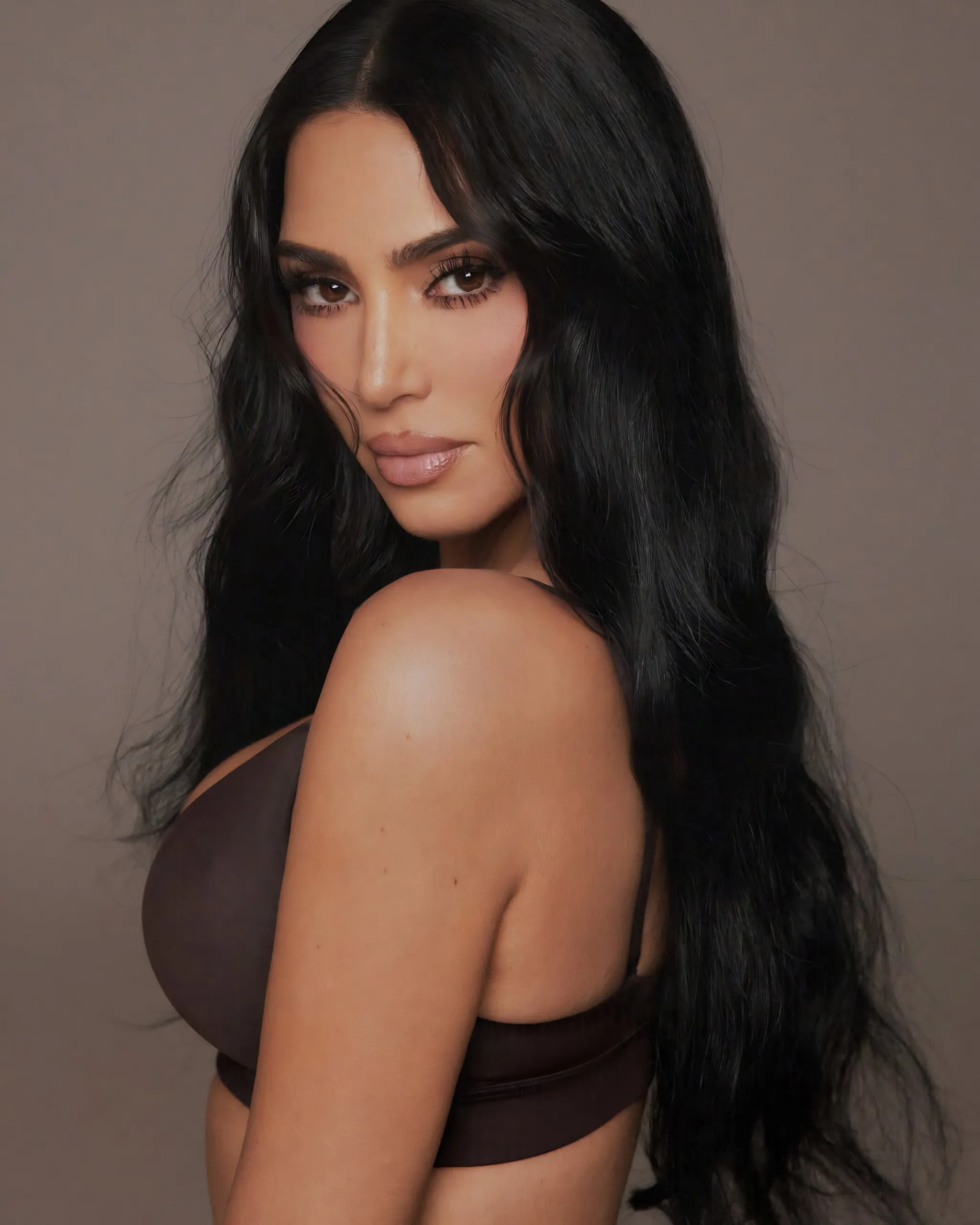 Side-profile of a woman with long black hair wearing a brown bra against a neutral backdrop, showing shoulders and partial torso.