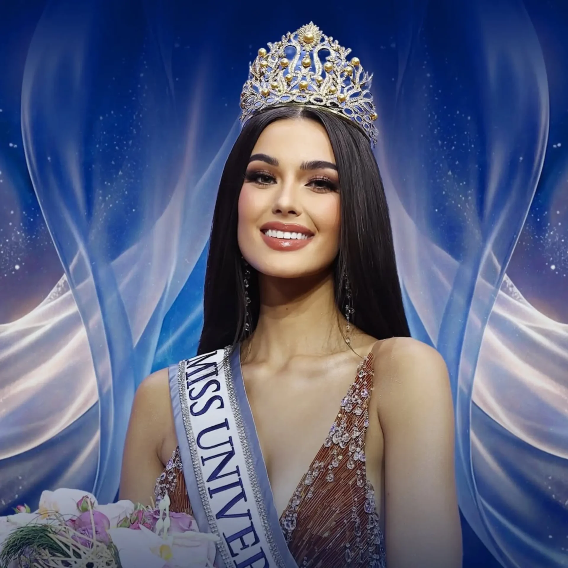 Beauty pageant winner wearing a jeweled crown and sash, smiling, with a bouquet in the foreground against a blue backdrop.