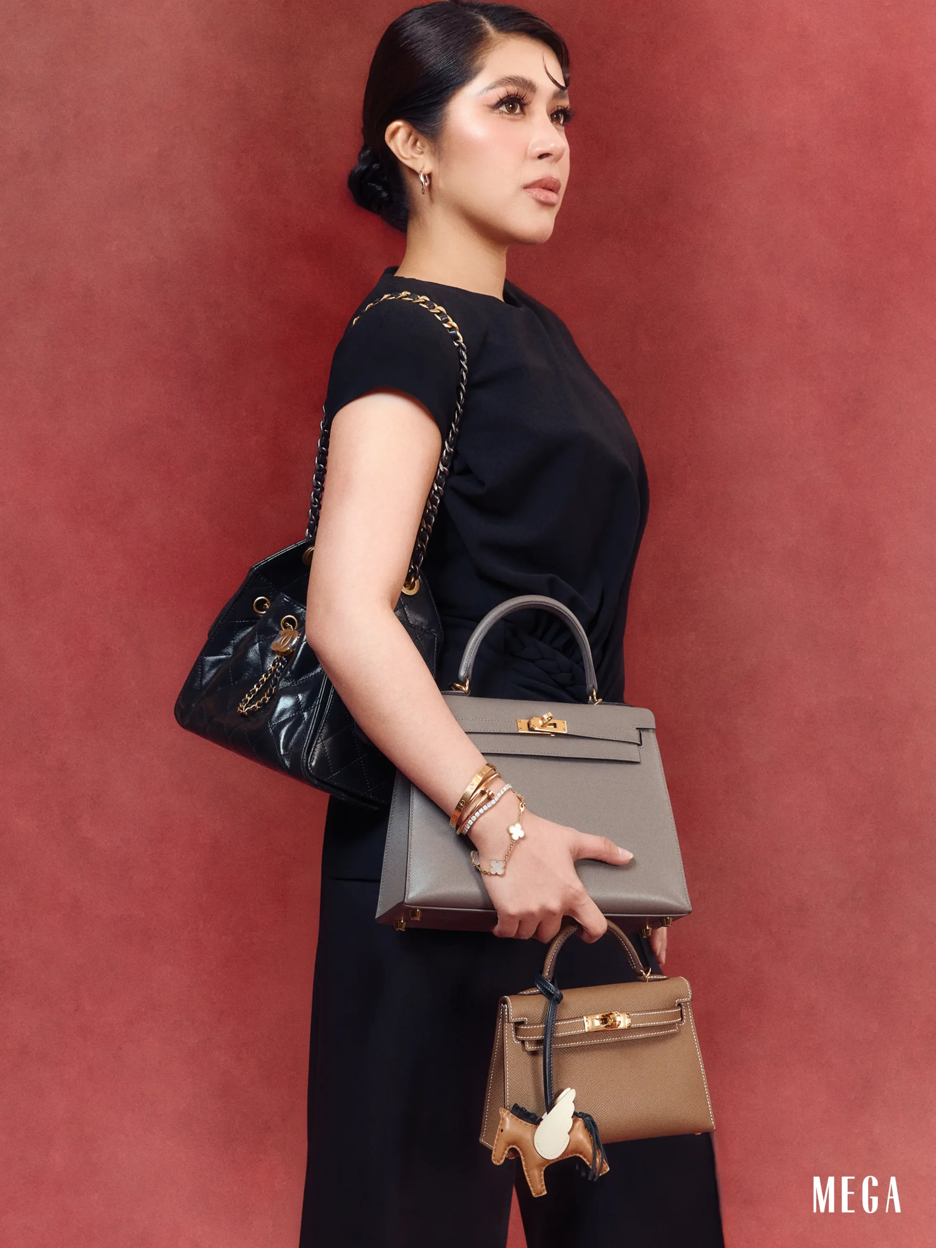 Woman in a black dress carries two handbags—a taupe structured bag and a black quilted bag with chain strap—against a red background