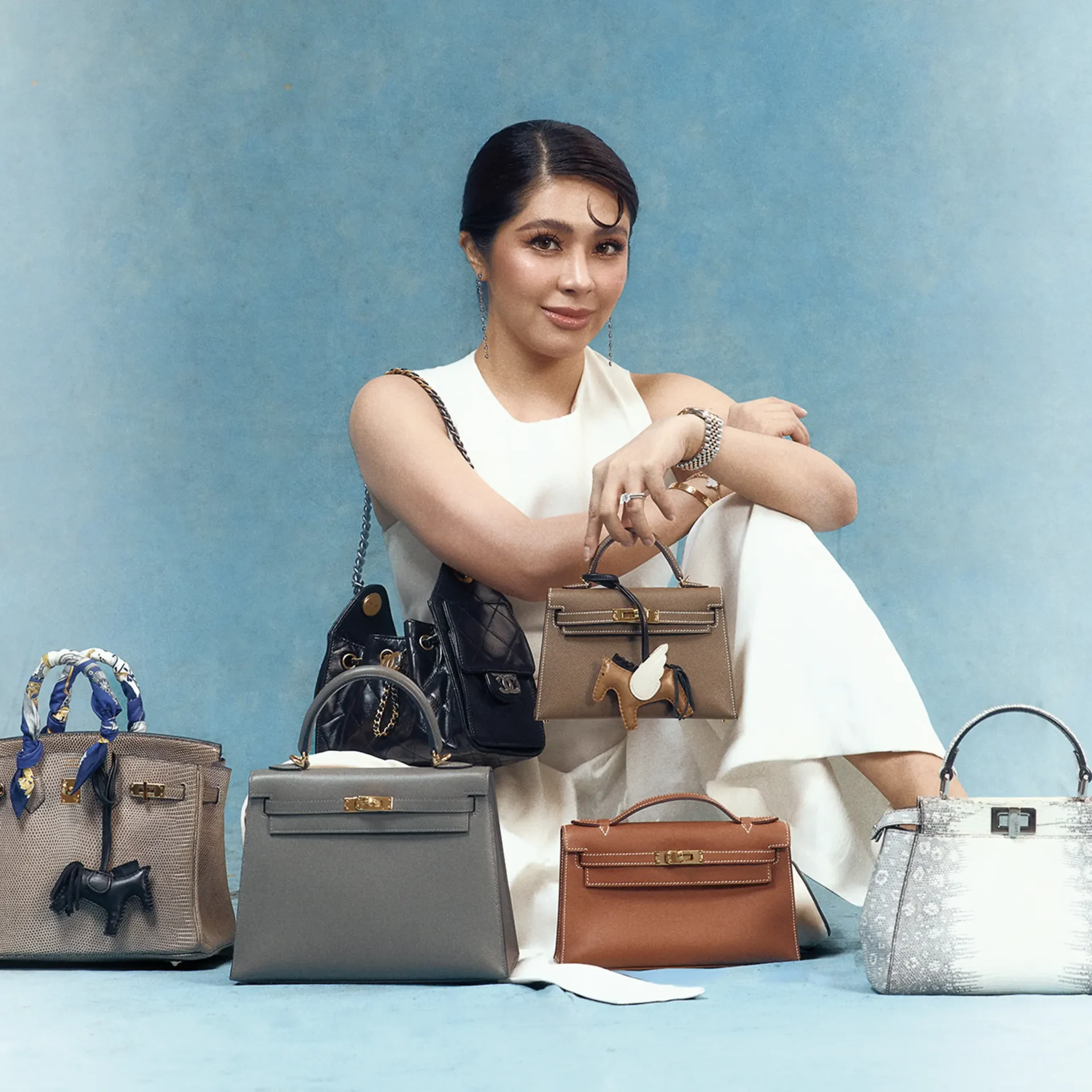 Row of designer handbags in beige, gray, and brown on a blue background.