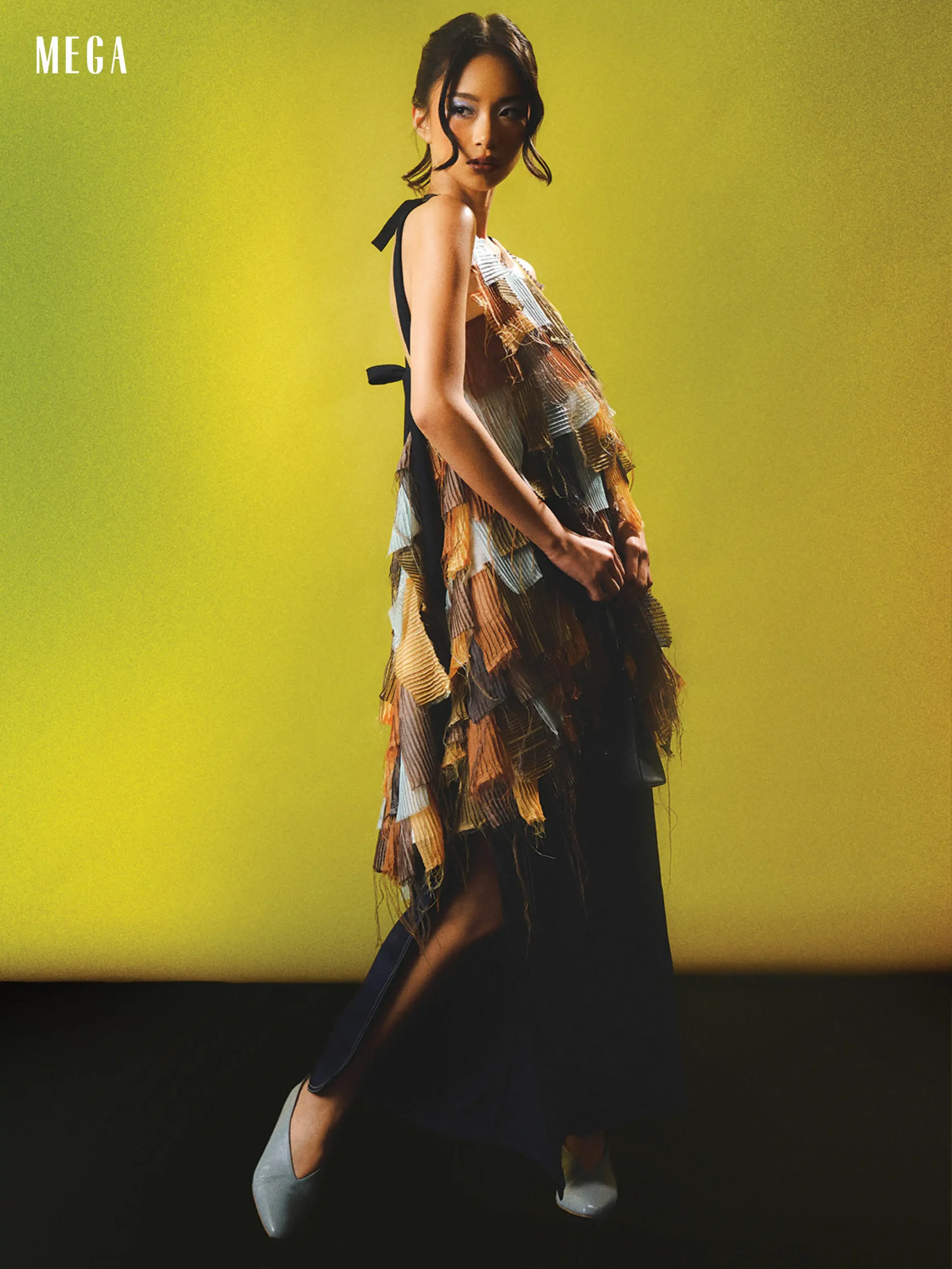 Model posing in a multi-layer fringe dress against a bright yellow backdrop; MEGA logo in the top-left corner.