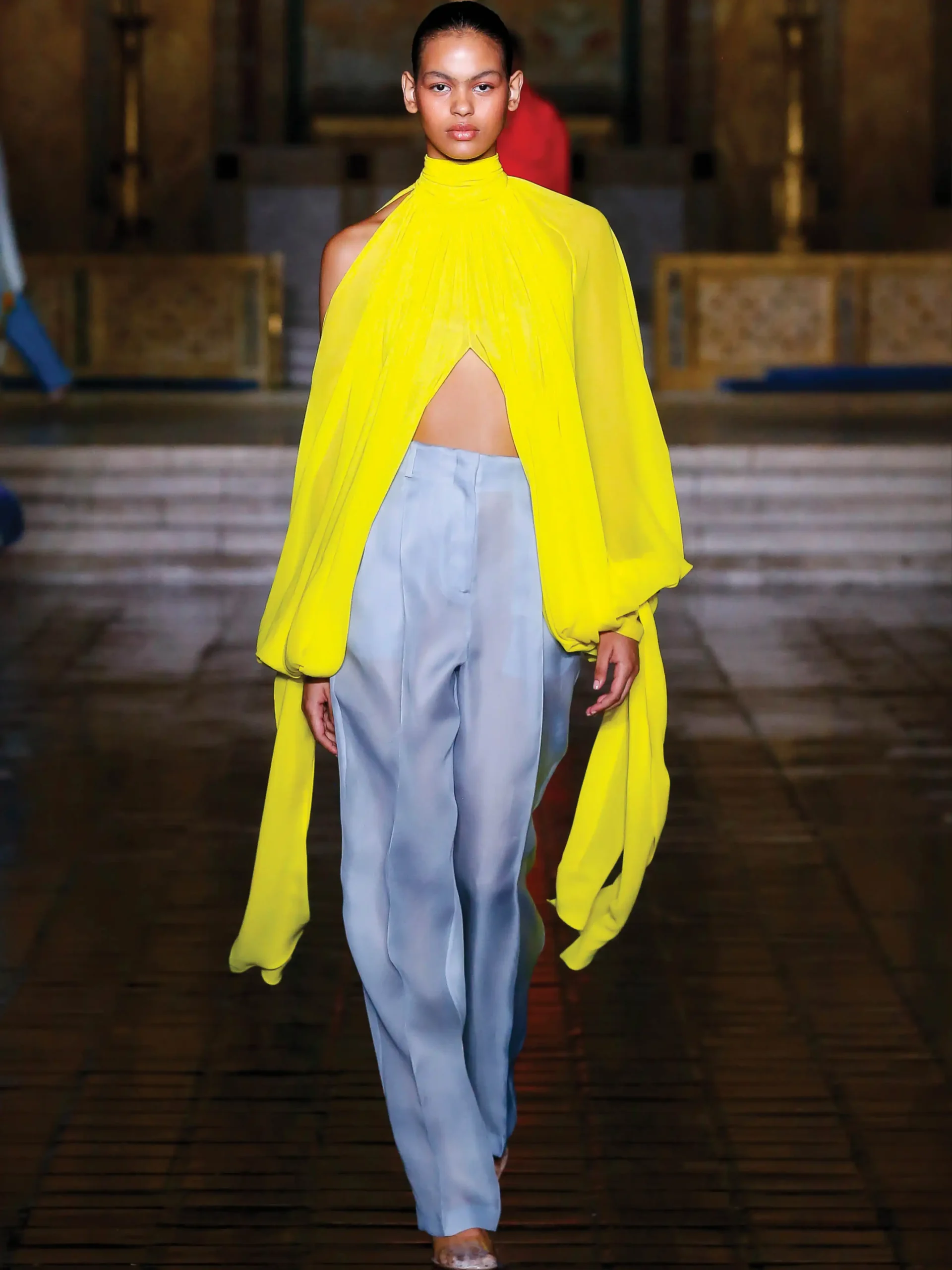 A model showcasing a Prabal Gurung ensemble featuring a vibrant citron chiffon top paired with baby blue trousers from the Spring/Summer 2026 collection.
