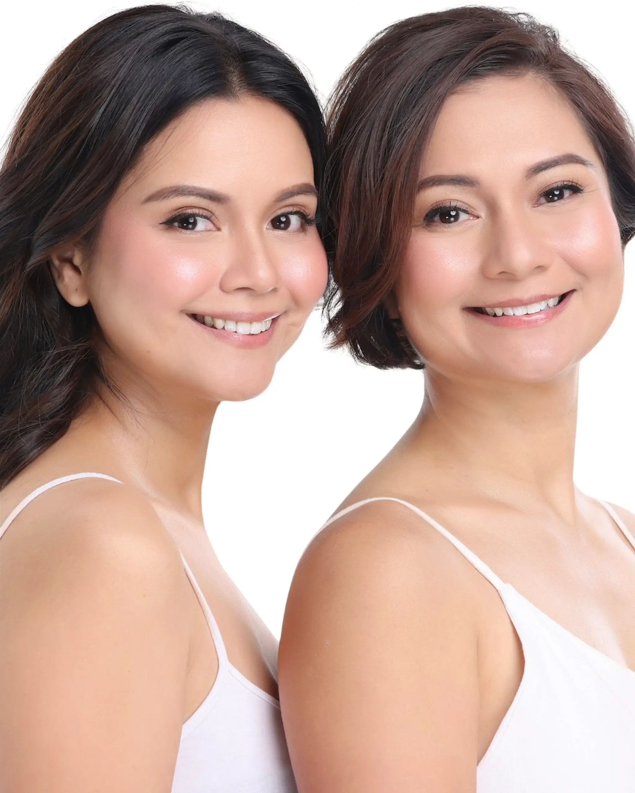 Two women smiling at the camera with their heads close together, wearing white tops.