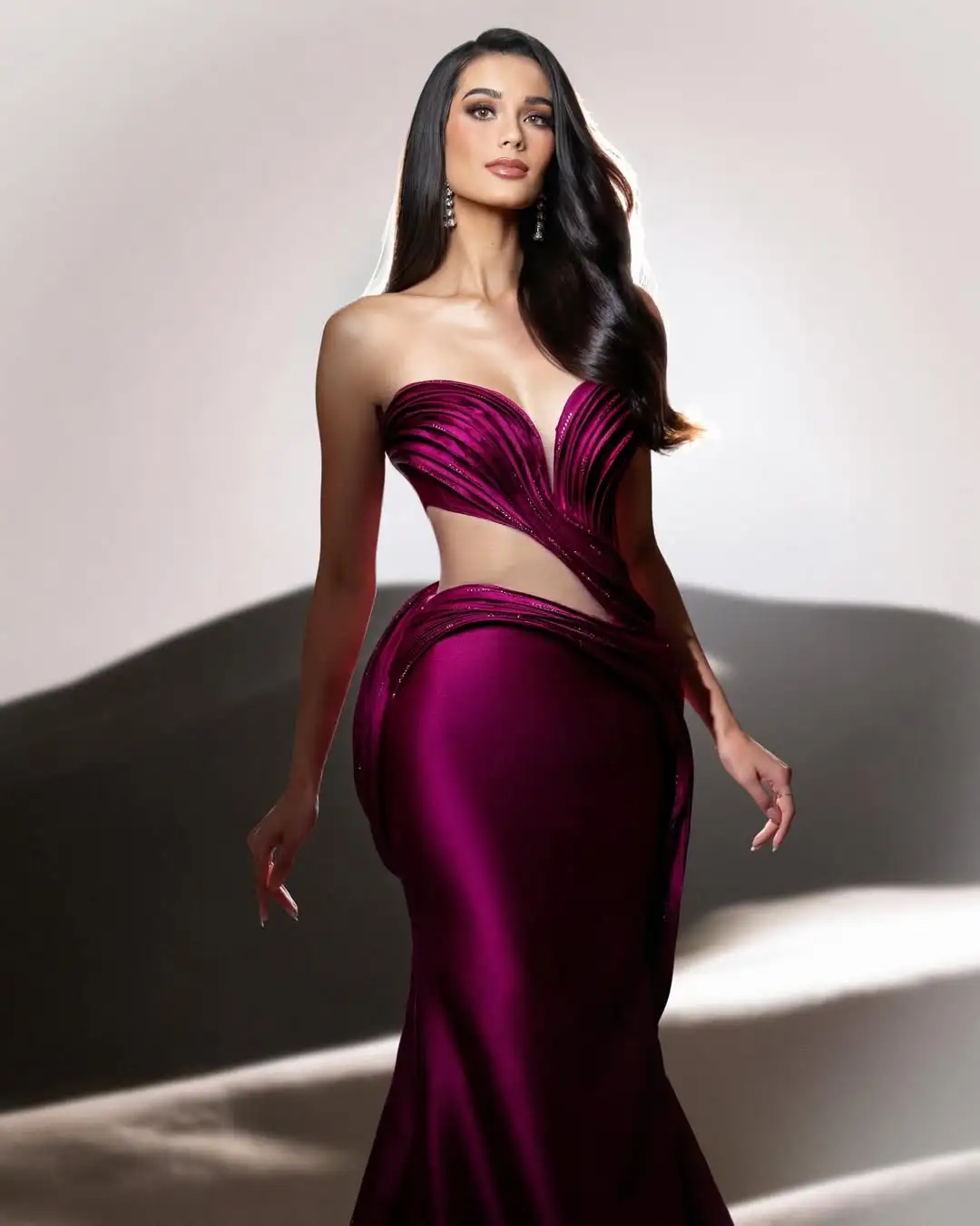 Model in a deep magenta strapless evening gown with a twisted bodice and side cutout, posing gracefully.