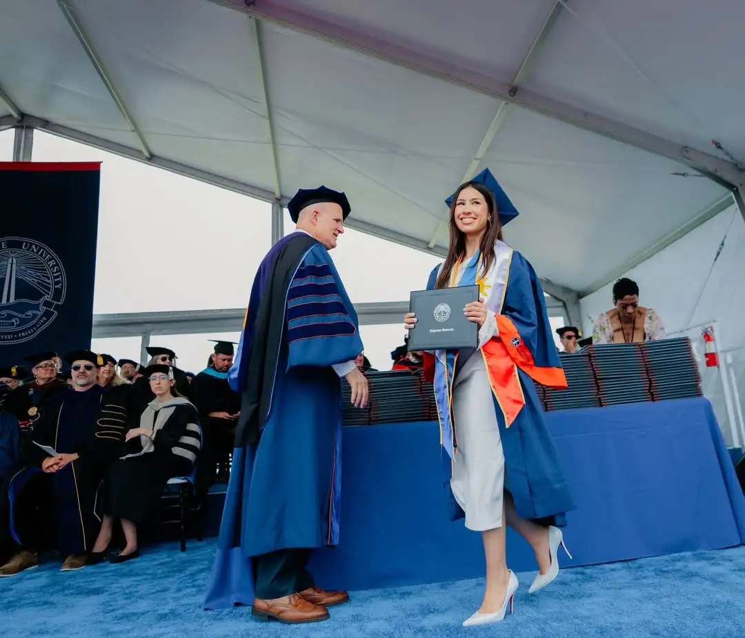 Lorin Gutierrez graduates in a blue cap and gown and receives a diploma from a faculty member.