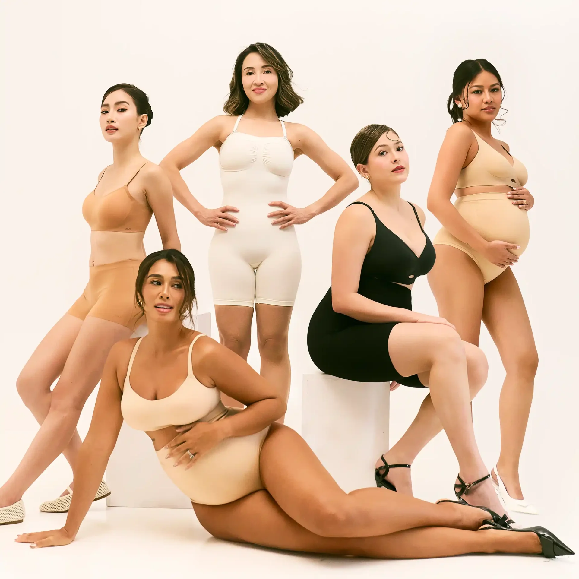 Group of diverse women posing in neutral-toned lingerie and bodysuits against a light background in a fashion shoot.