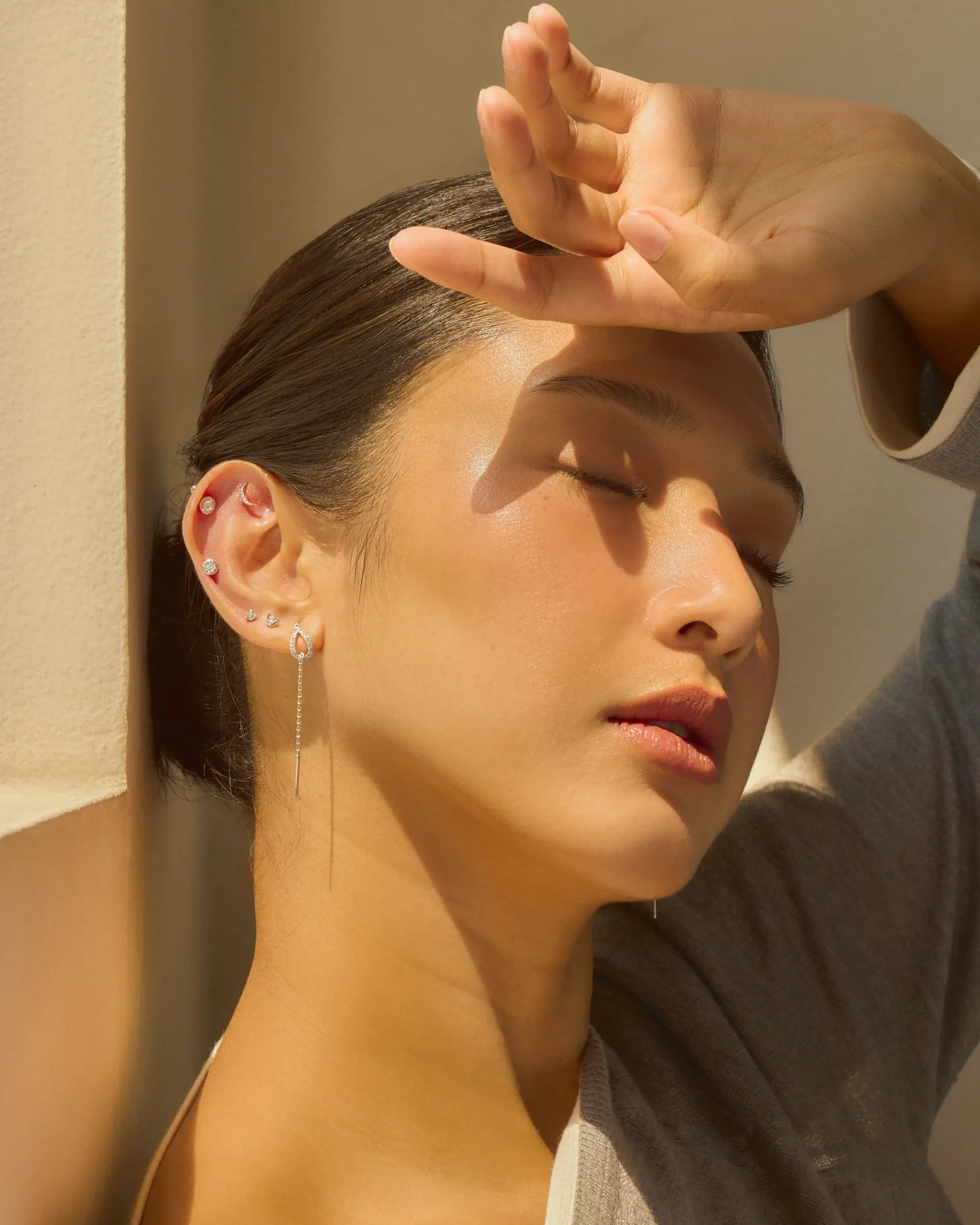 Close-up of a woman shielding her eyes from the sun with her hand raised above her forehead, wearing multiple earrings. All Day, All Night: Suki Jewelry Tells Time Differently