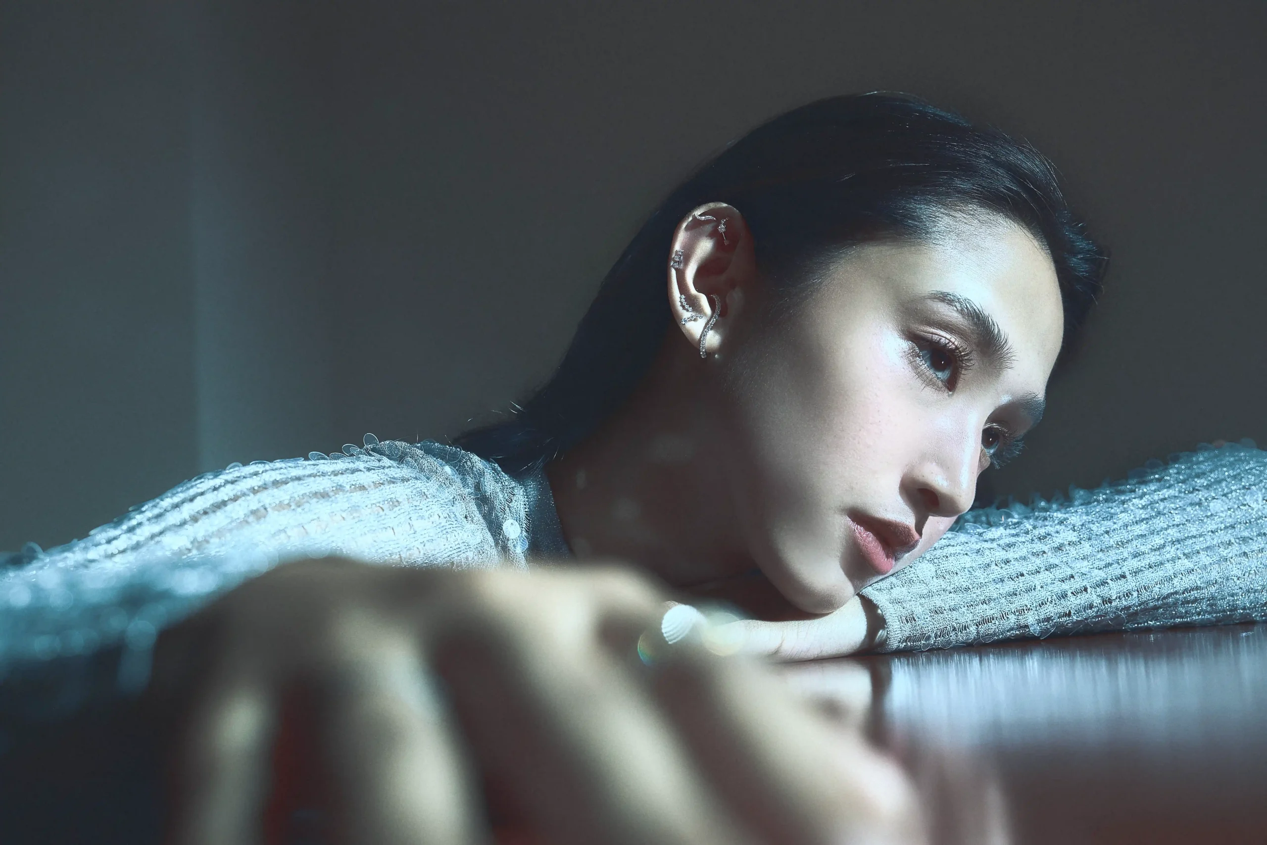 Close-up of a woman resting her face on a textured blue surface, showcasing a silver earring and moody blue lighting.