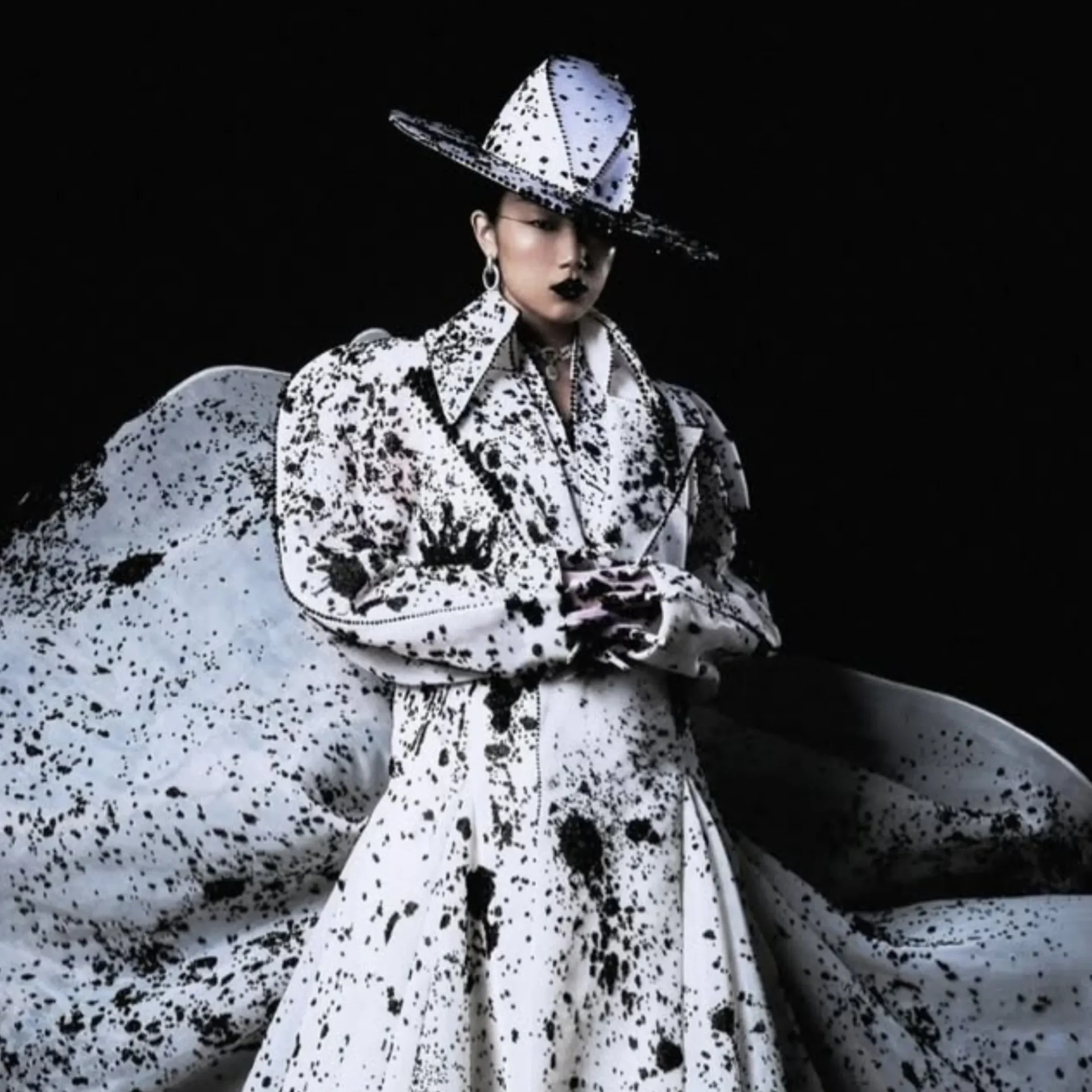 Model in a white speckled outfit and hat, against a black background.