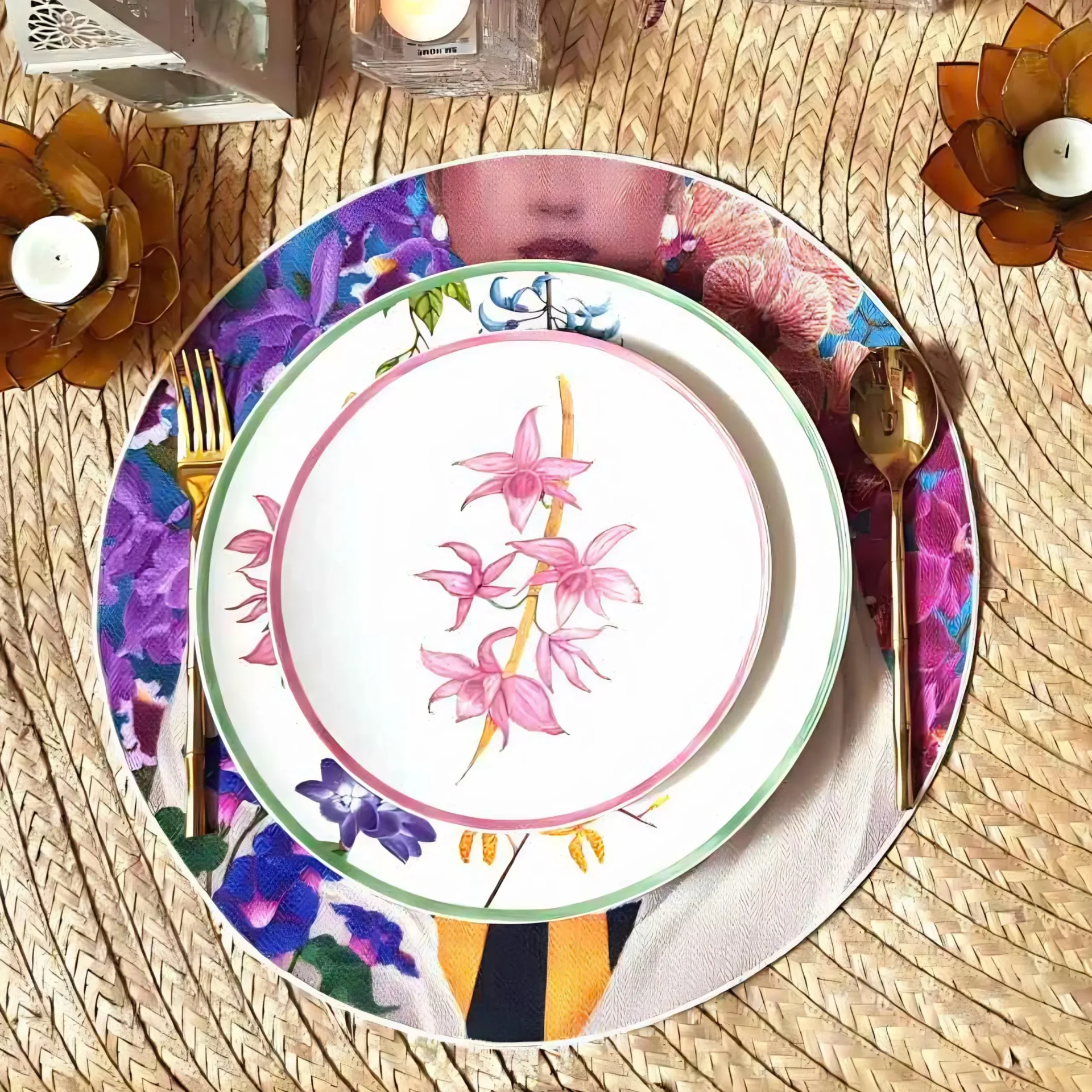Top-down view of a colorful stack of decorative plates on a woven mat, surrounded by napkins and plant-like decorations.