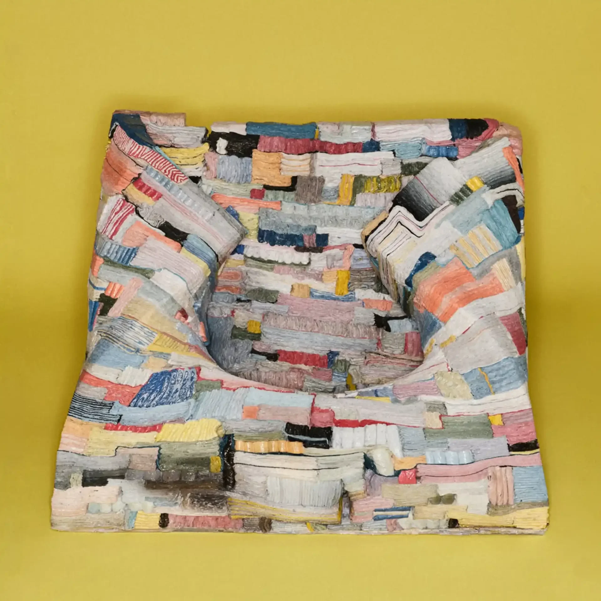 Patchwork quilt with colorful fabric strips draped over a chair against a bright yellow wall.