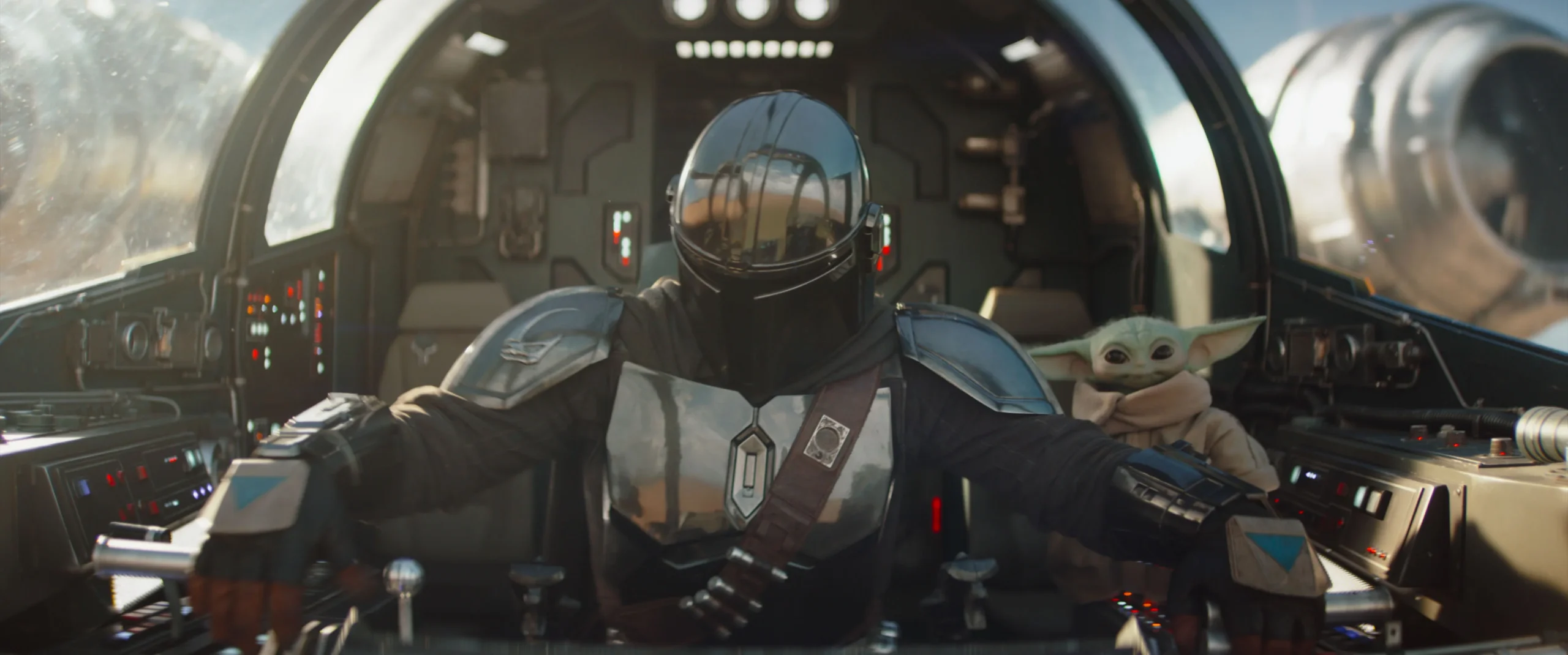 The Mandalorian pilot controls a spaceship from the cockpit with Grogu sitting closely by his side.