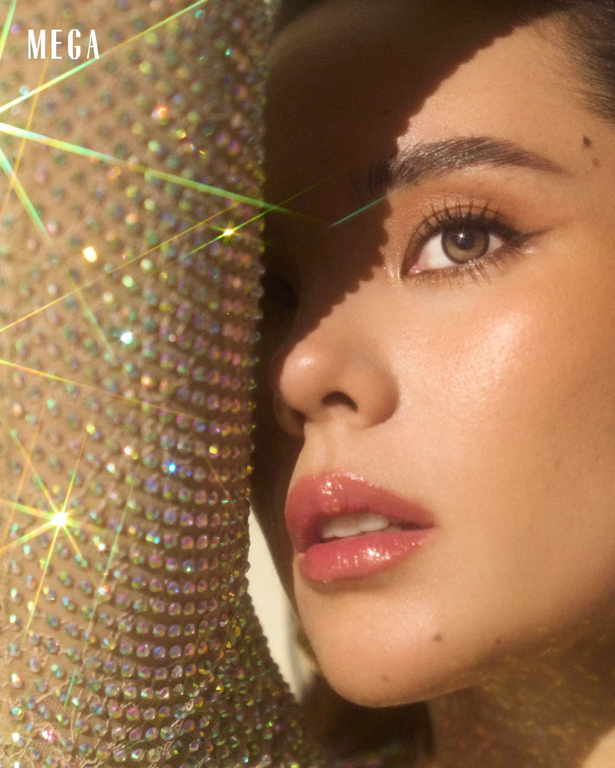 Close-up of a woman's face showing eye makeup and glossy lips, set against a sparkling sequin background.