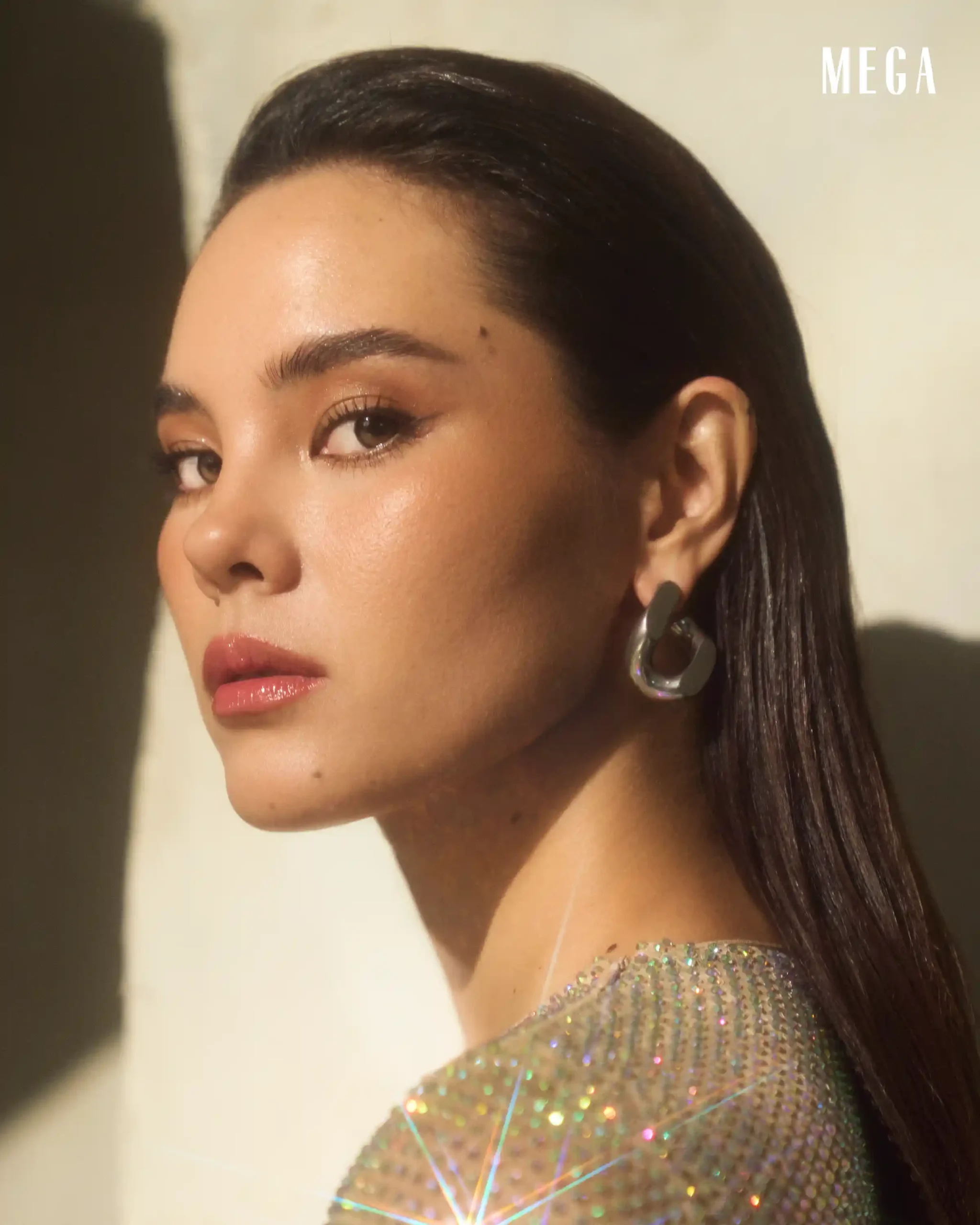 Close-up profile of a woman with glossy lips, bold eye makeup, and a large hoop earring, wearing a shimmering dress; MEGA watermark in corner.