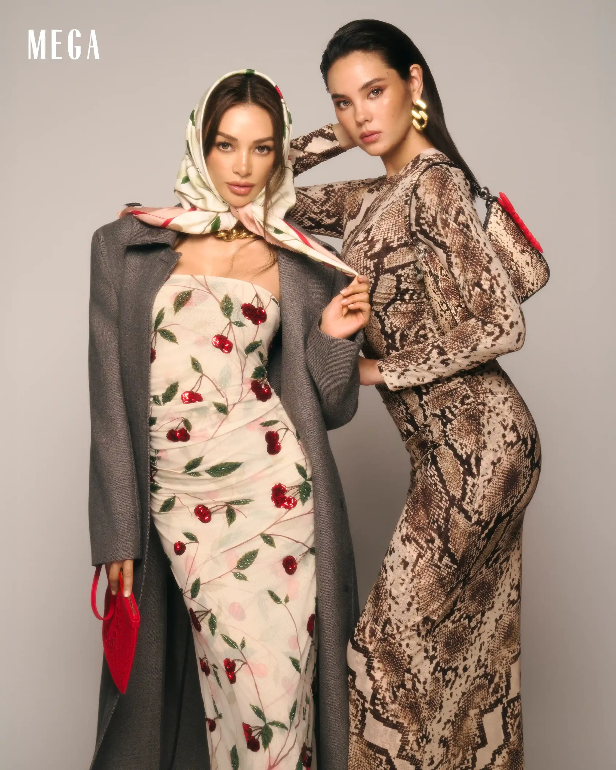 Two fashion models pose together against a plain backdrop: one in a cherry-printed dress with a scarf and gray coat, the other in a snakeskin dress, holding a red bag. MEGA logo in the corner.