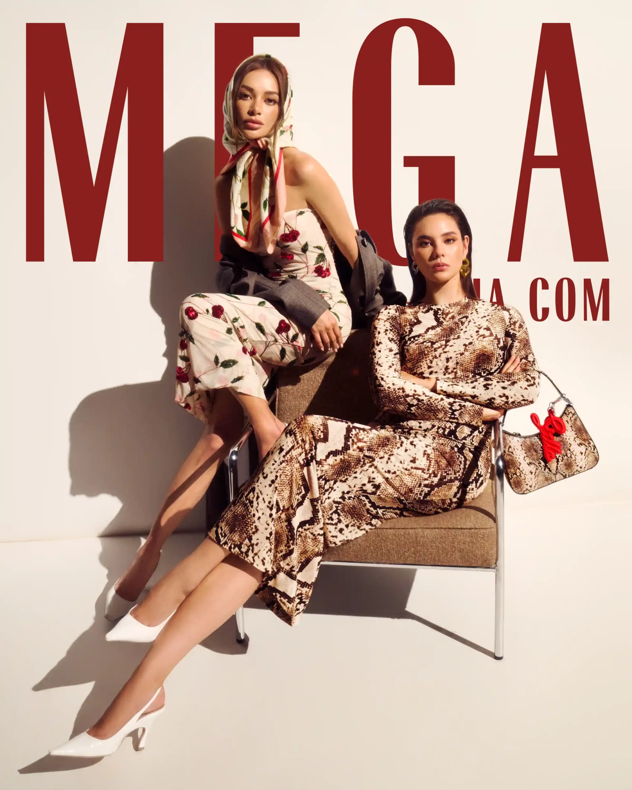 Two models pose on a chair against a beige backdrop with oversized red letters in the background, wearing floral and snakeskin outfits with white heels.