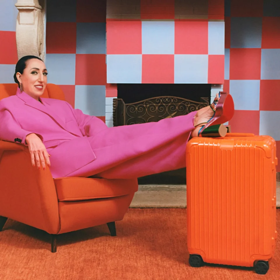 Actress Rossy de Palma, clad in bright magenta, lounging by her Orange Essential baggage