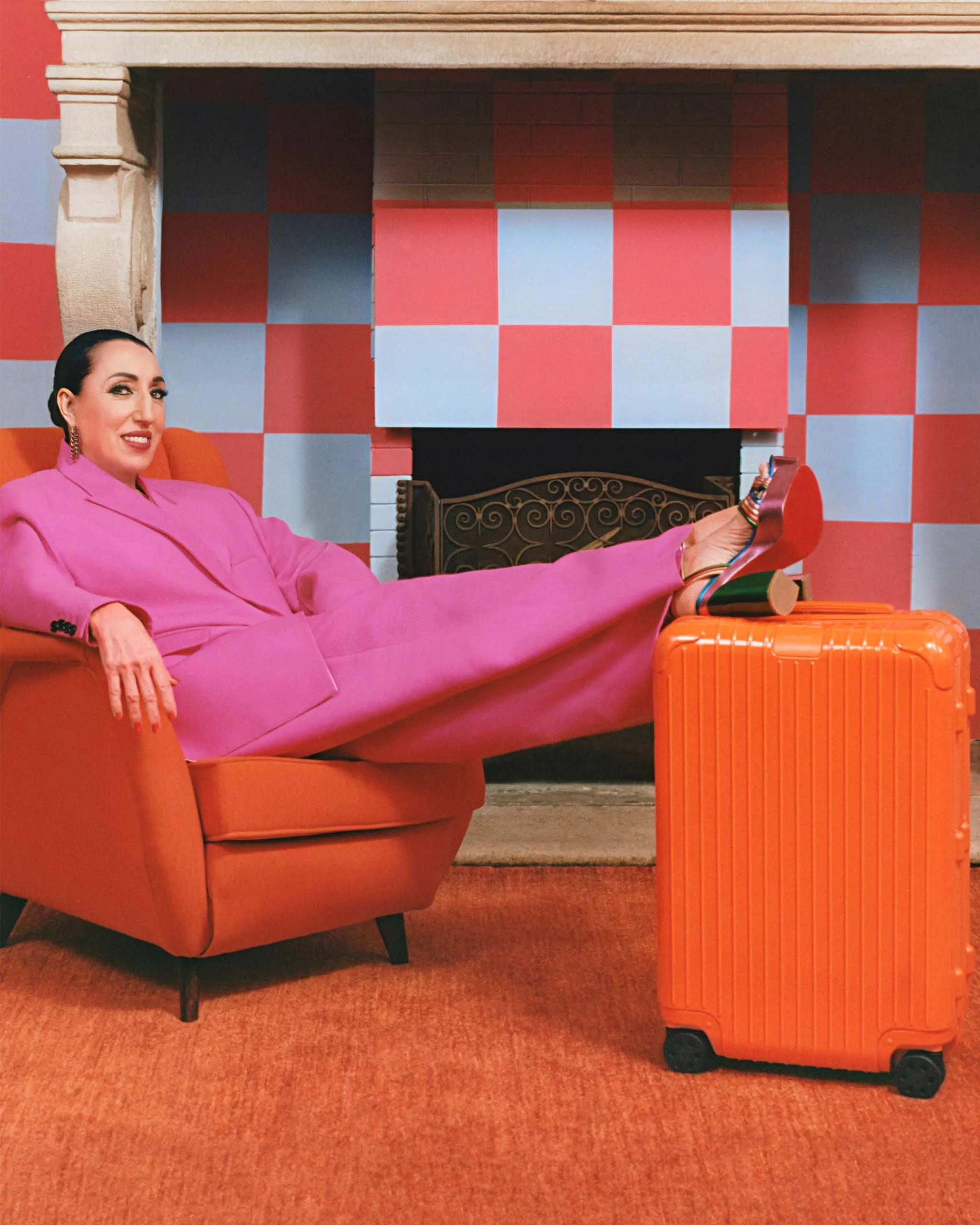 Actress Rossy de Palma, clad in bright magenta, lounging by her Orange Essential baggage