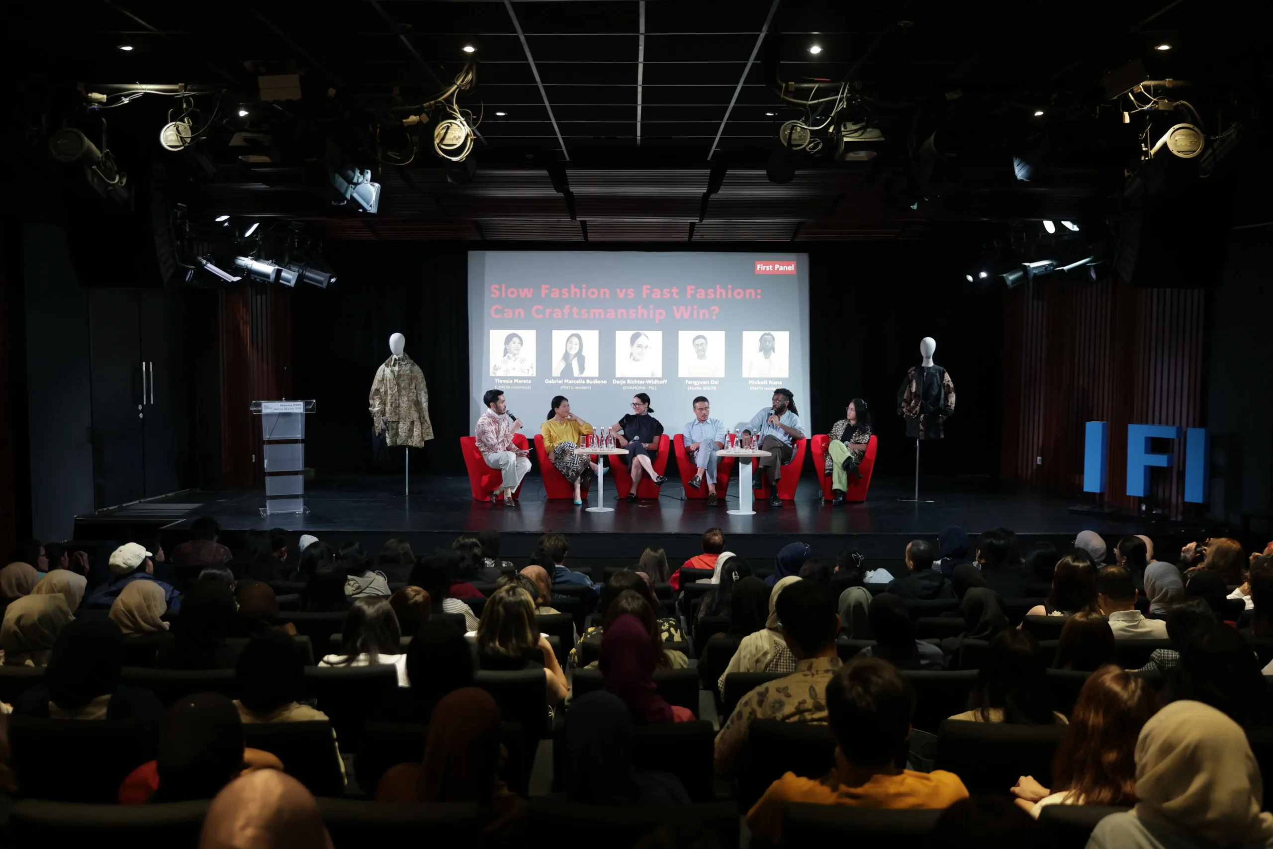 Panel on a stage with red chairs and six speakers; projection screen behind reads 'Slow Fashion vs Fast Fashion: Can Craftsmanship Win?'